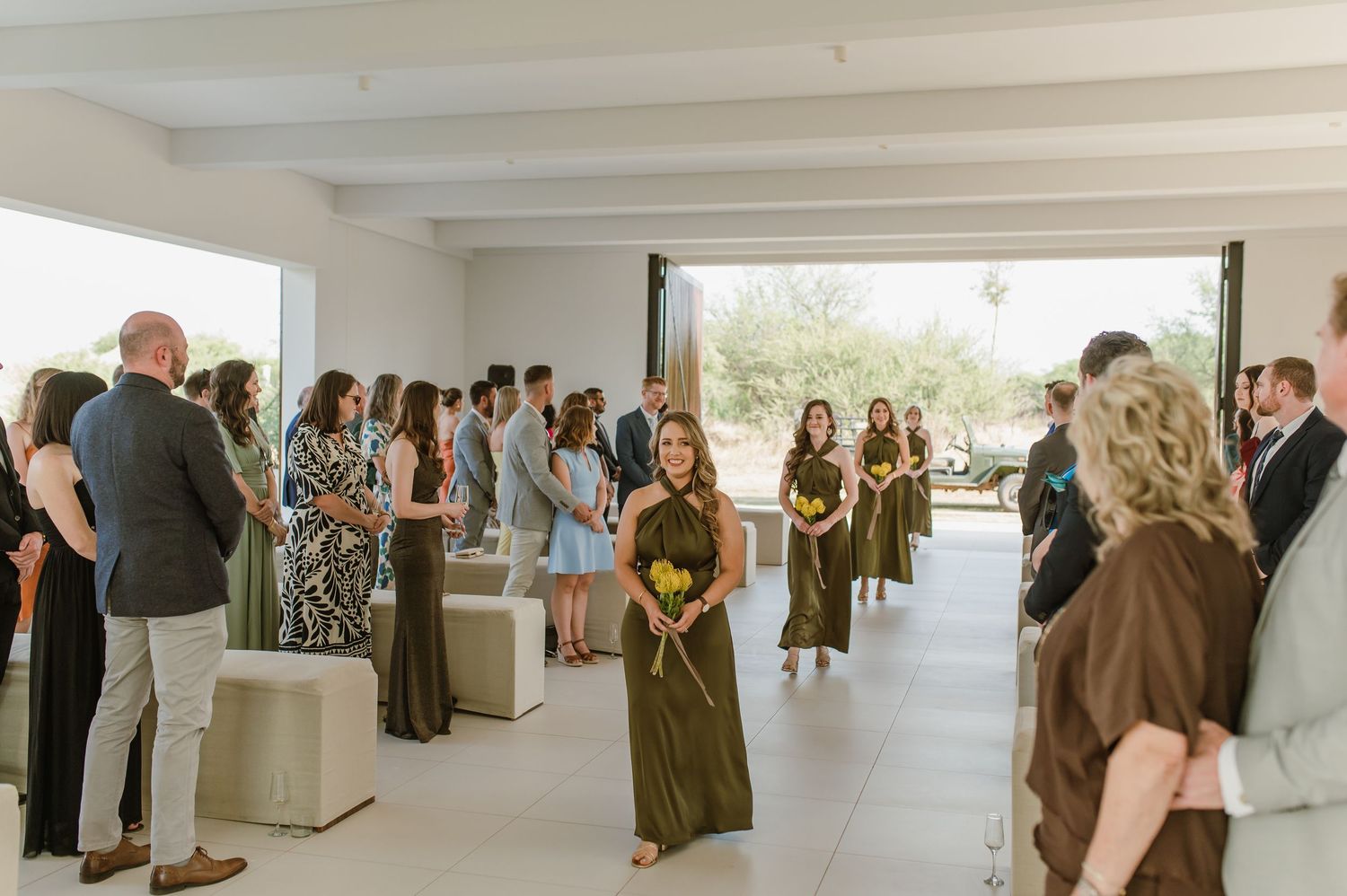 Wedding guests mingle in an elegant white-walled venue with natural lighting.