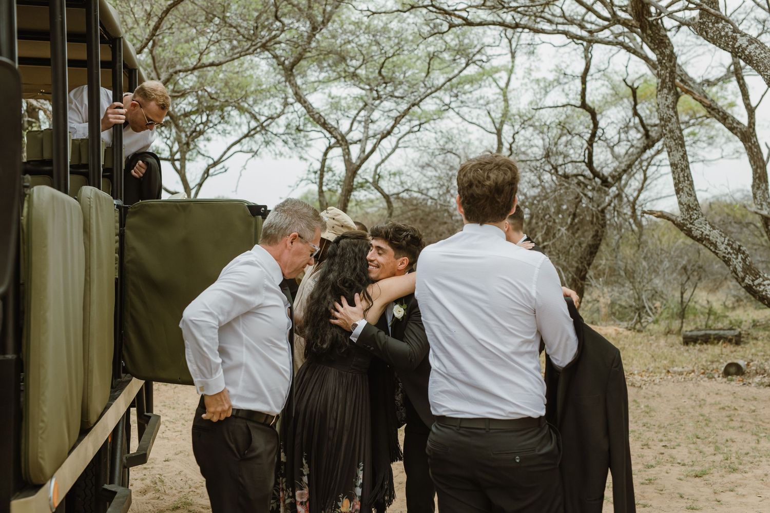 Wedding guests gather outside under trees during an outdoor ceremony.