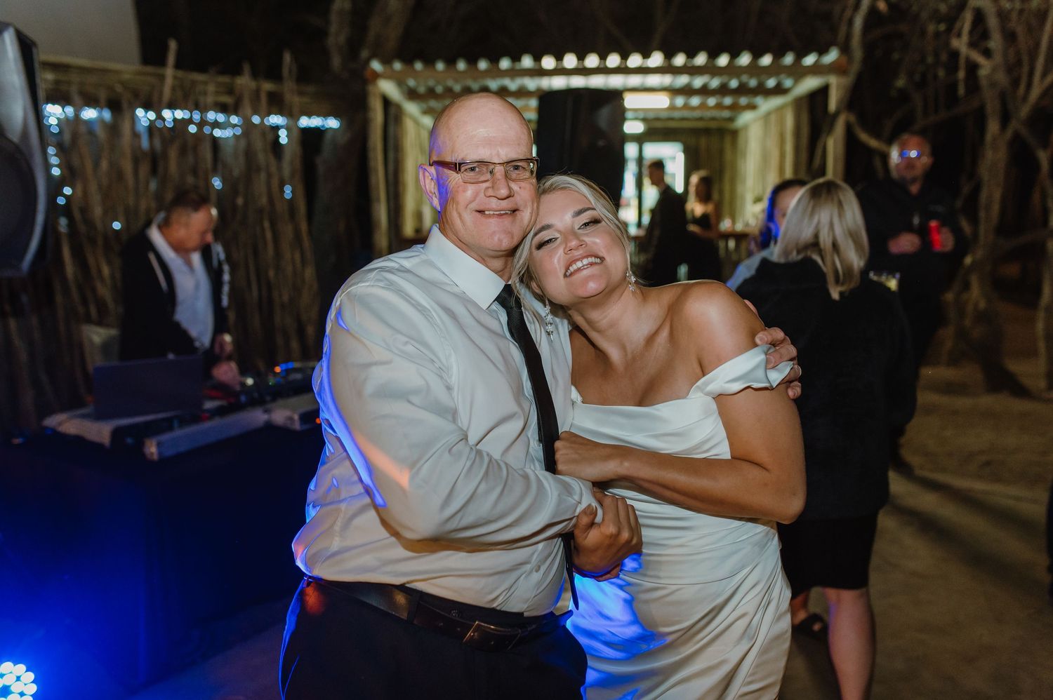 Couples dancing together at a dimly lit wedding reception venue with string lights overhead.