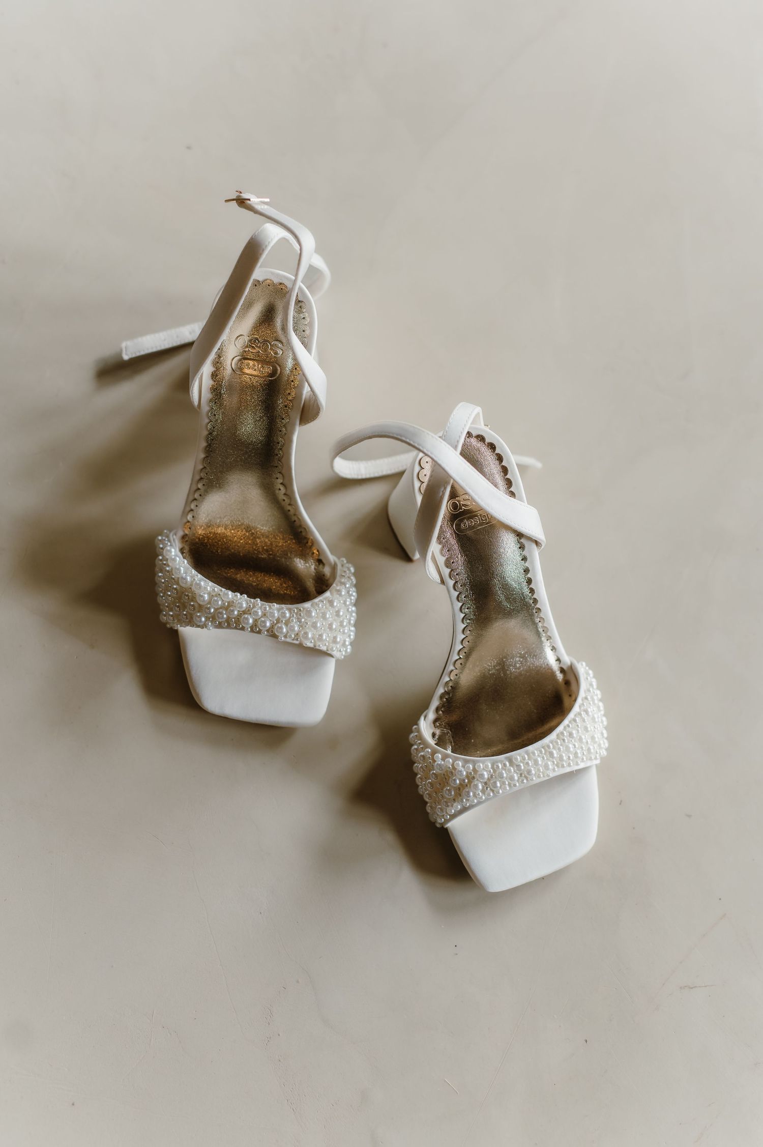 Elegant white bridal heels with crystal embellishments on neutral background.