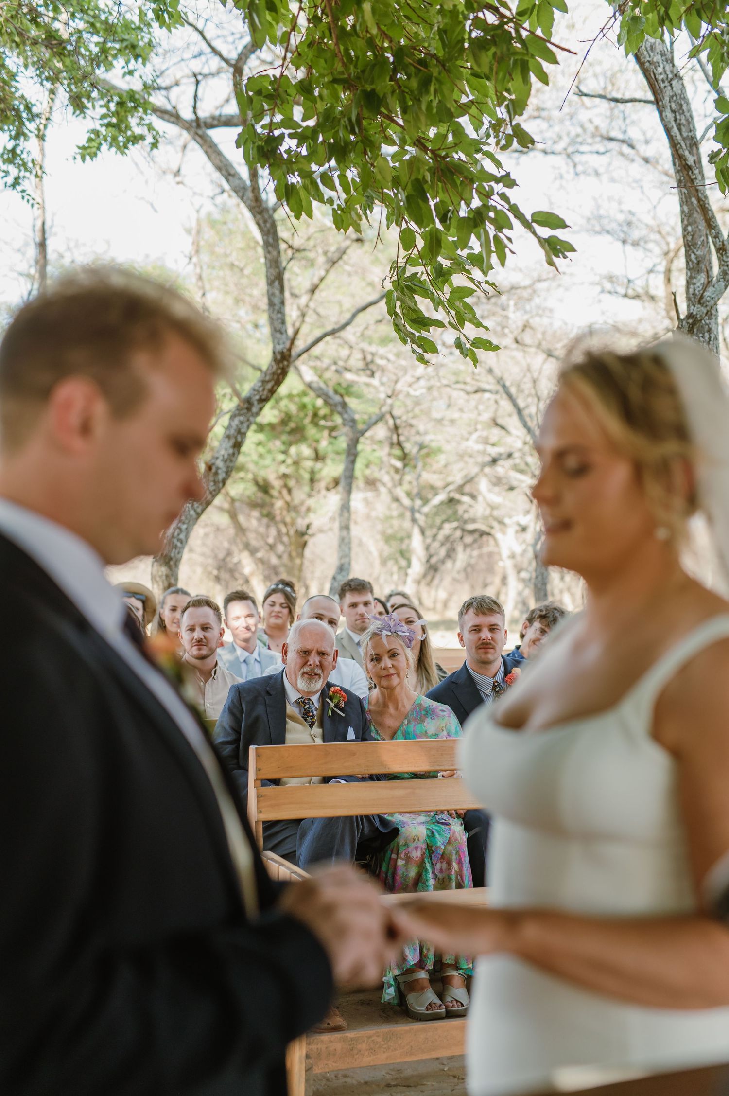 Couple exchanges rings during intimate outdoor wedding ceremony with wooden benches.