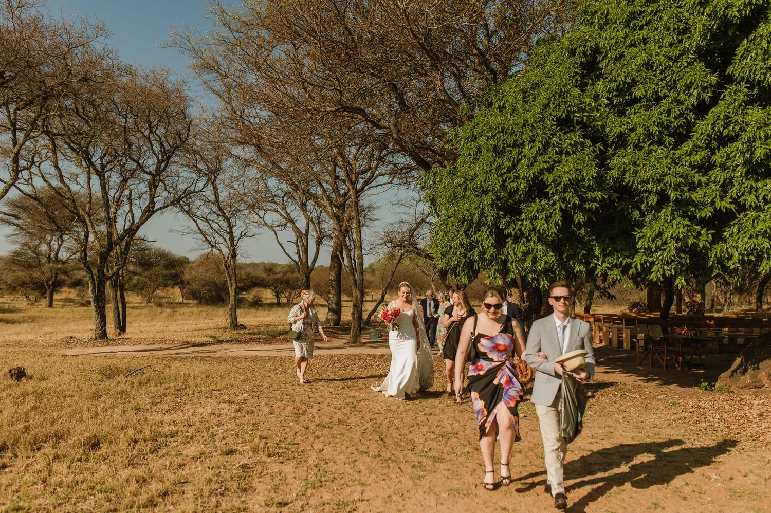 Scenic outdoor wedding venue with guests mingling among desert trees.