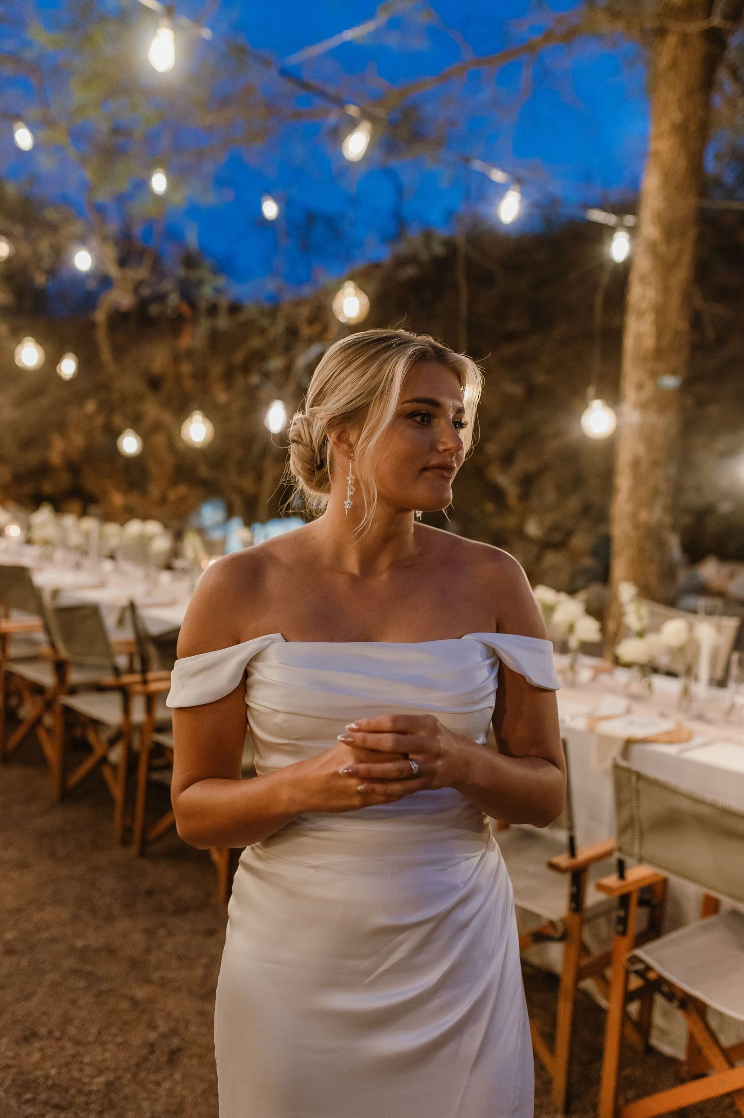 Evening wedding reception space with elegant table settings under warm string lights.