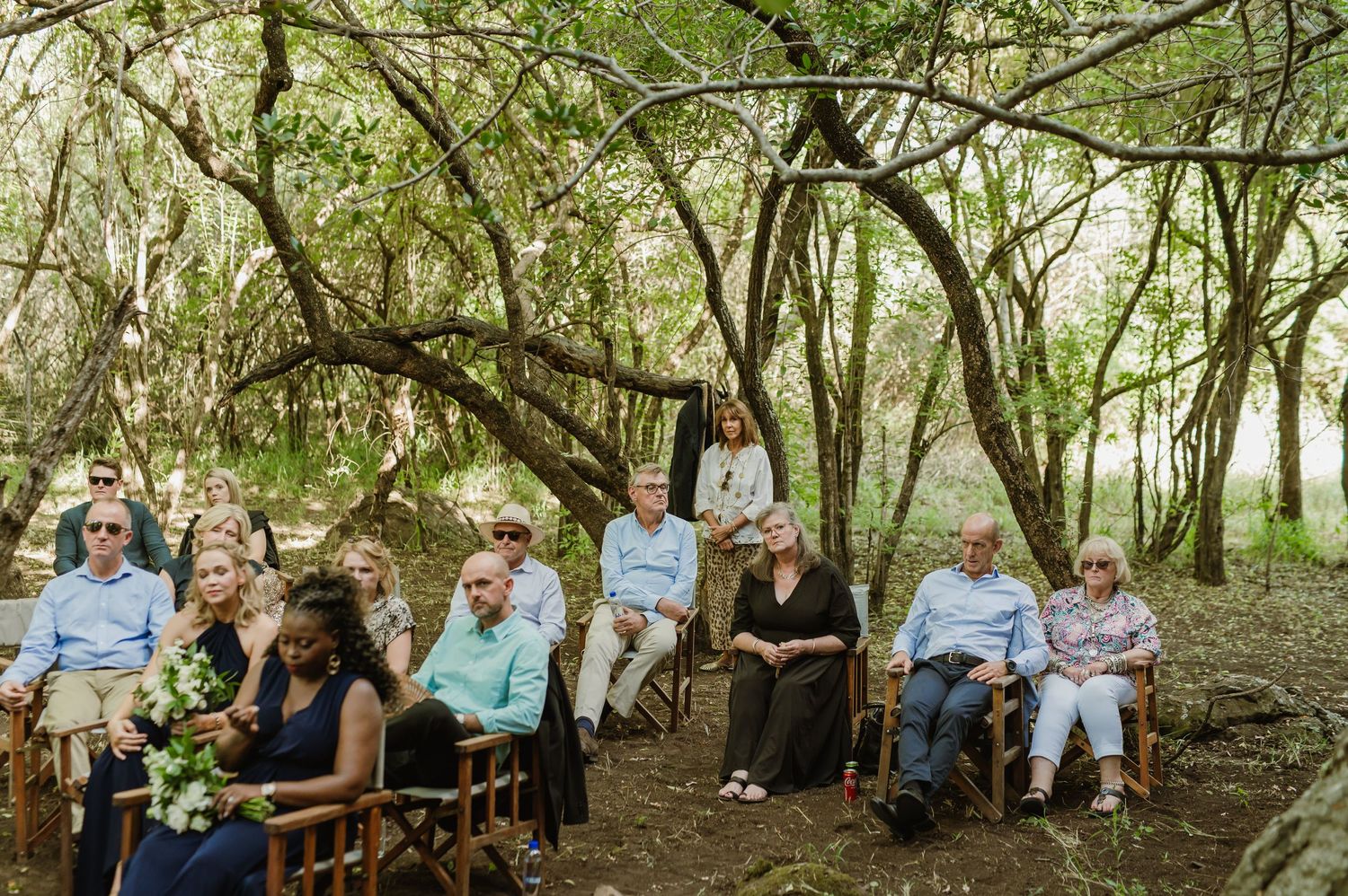 Wedding guests seated on wooden benches in natural forest amphitheater setting.