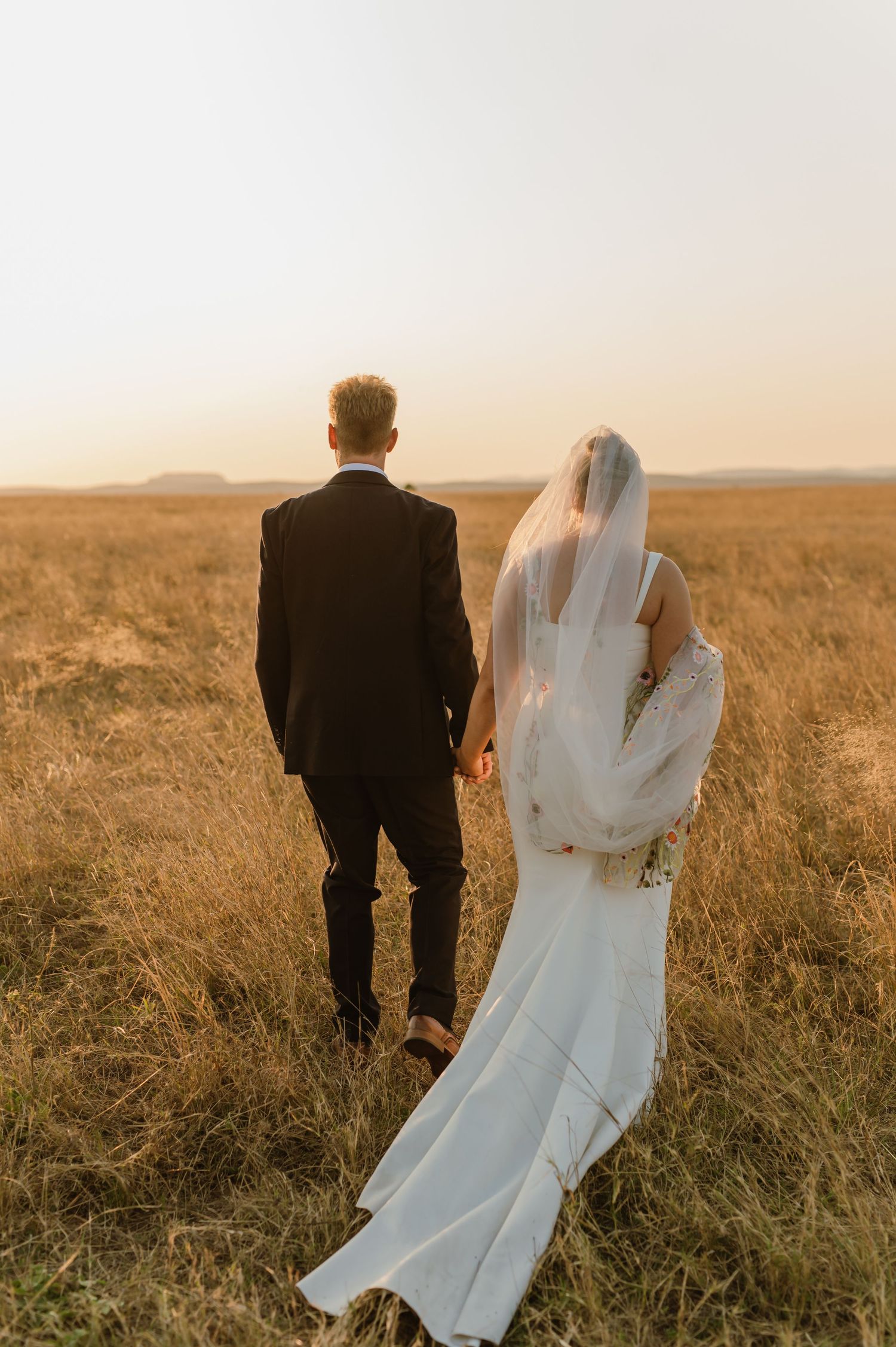 A couple walks through a golden field during their sunset wedding photography session.