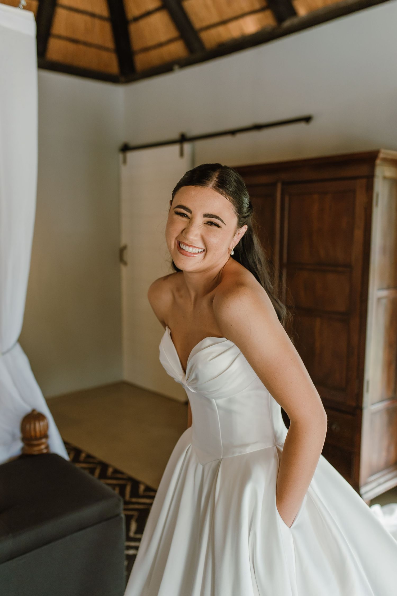 Radiant bride in strapless white ball gown smiling over her shoulder in a rustic wedding suite.