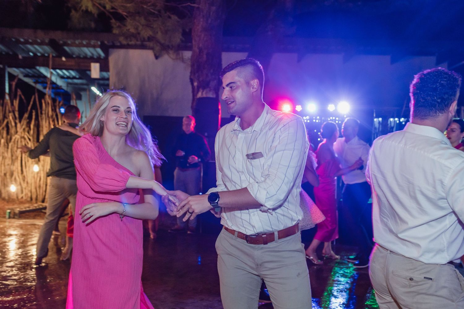 Couple in pink dress and khakis dance together joyfully at lively outdoor wedding reception.