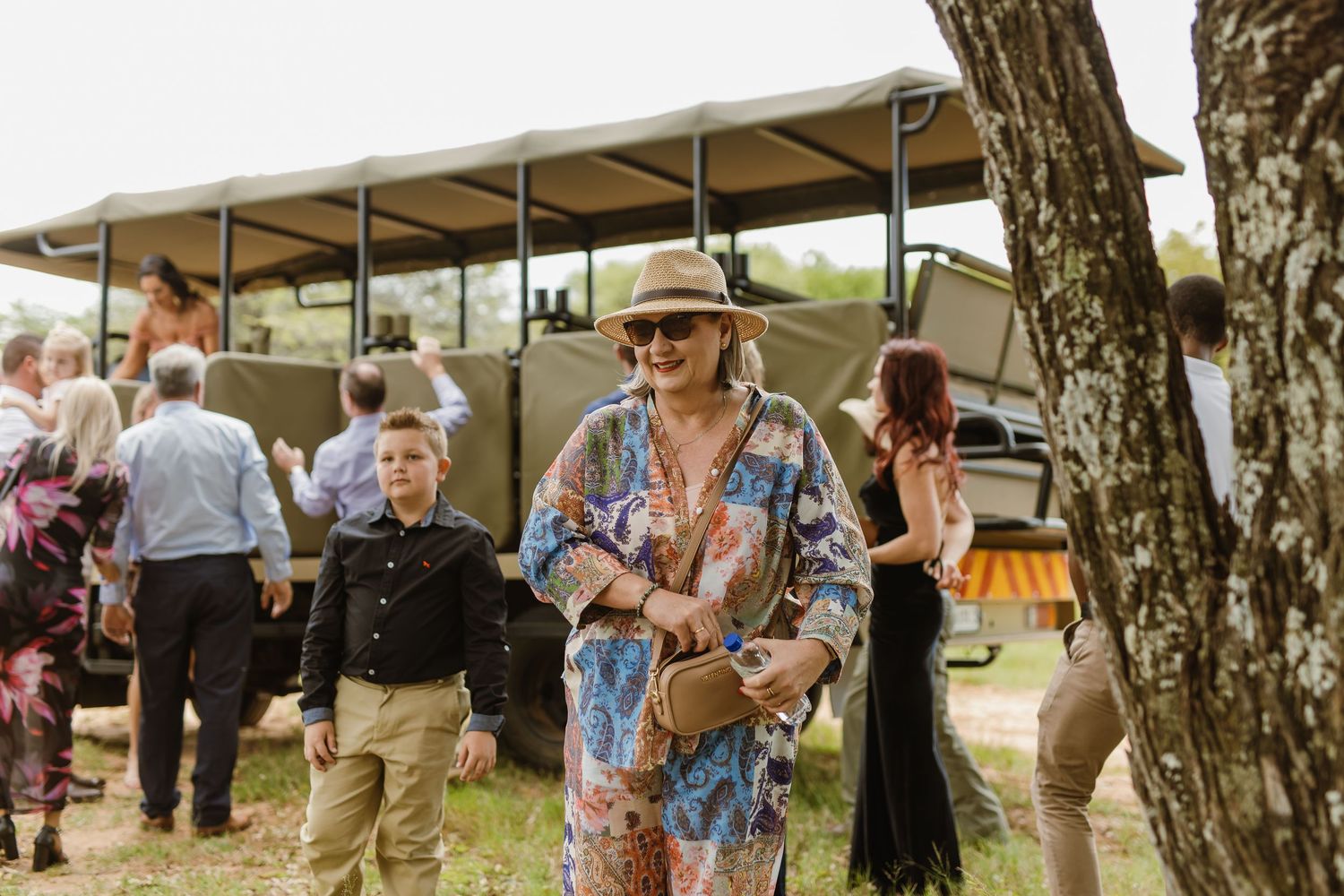 Wedding guest in floral outfit and sun hat walking near safari tent at outdoor bush wedding.