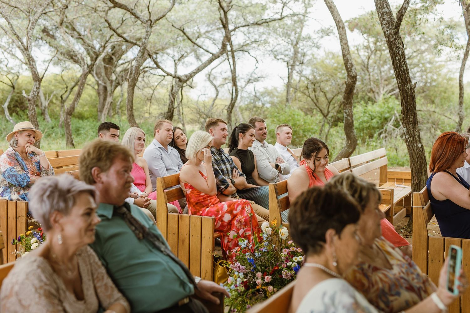Wedding guests seated on wooden benches at an outdoor bush wedding ceremony.
