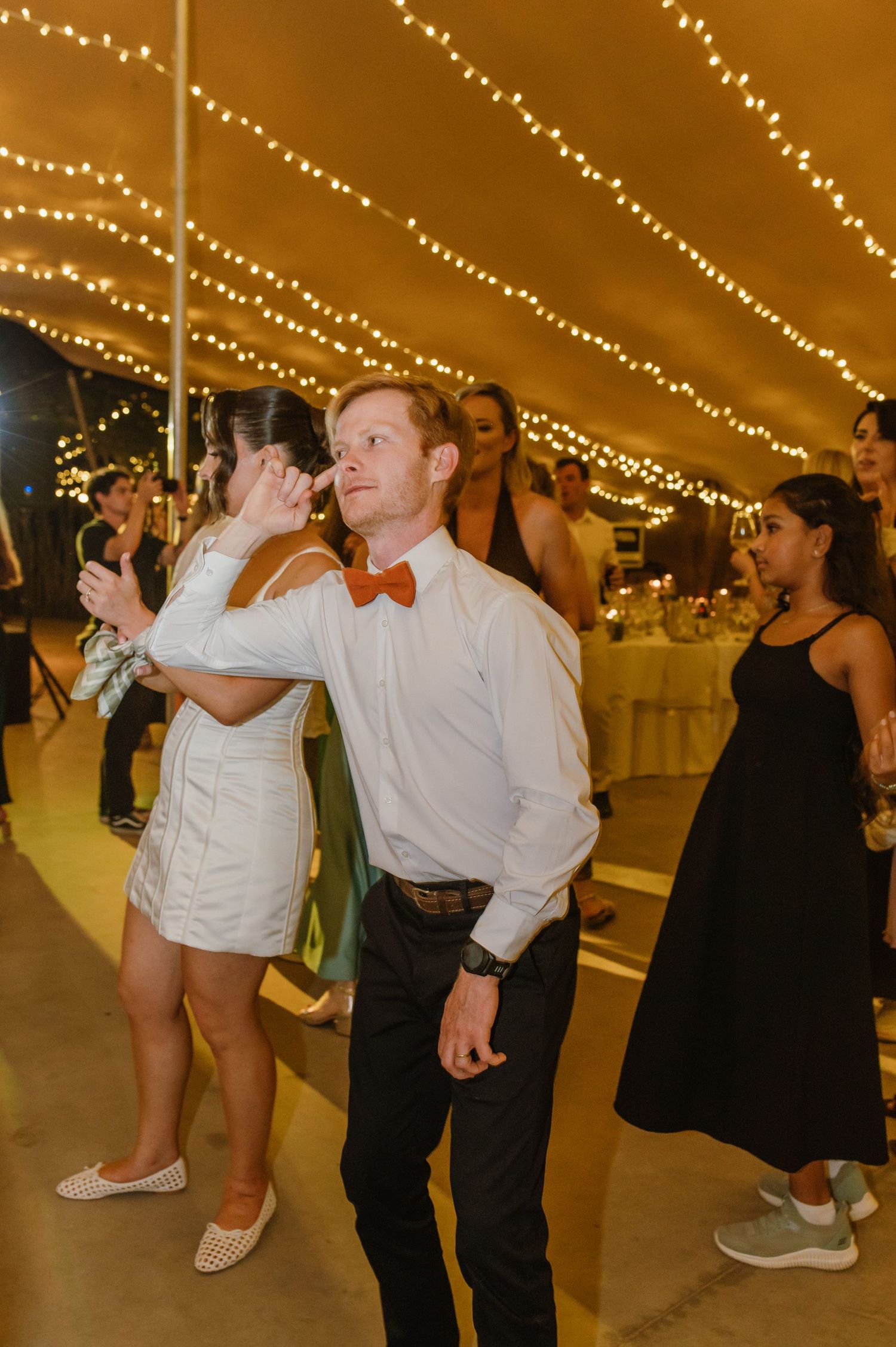 Wedding reception dance floor with guests celebrating under string lights.
