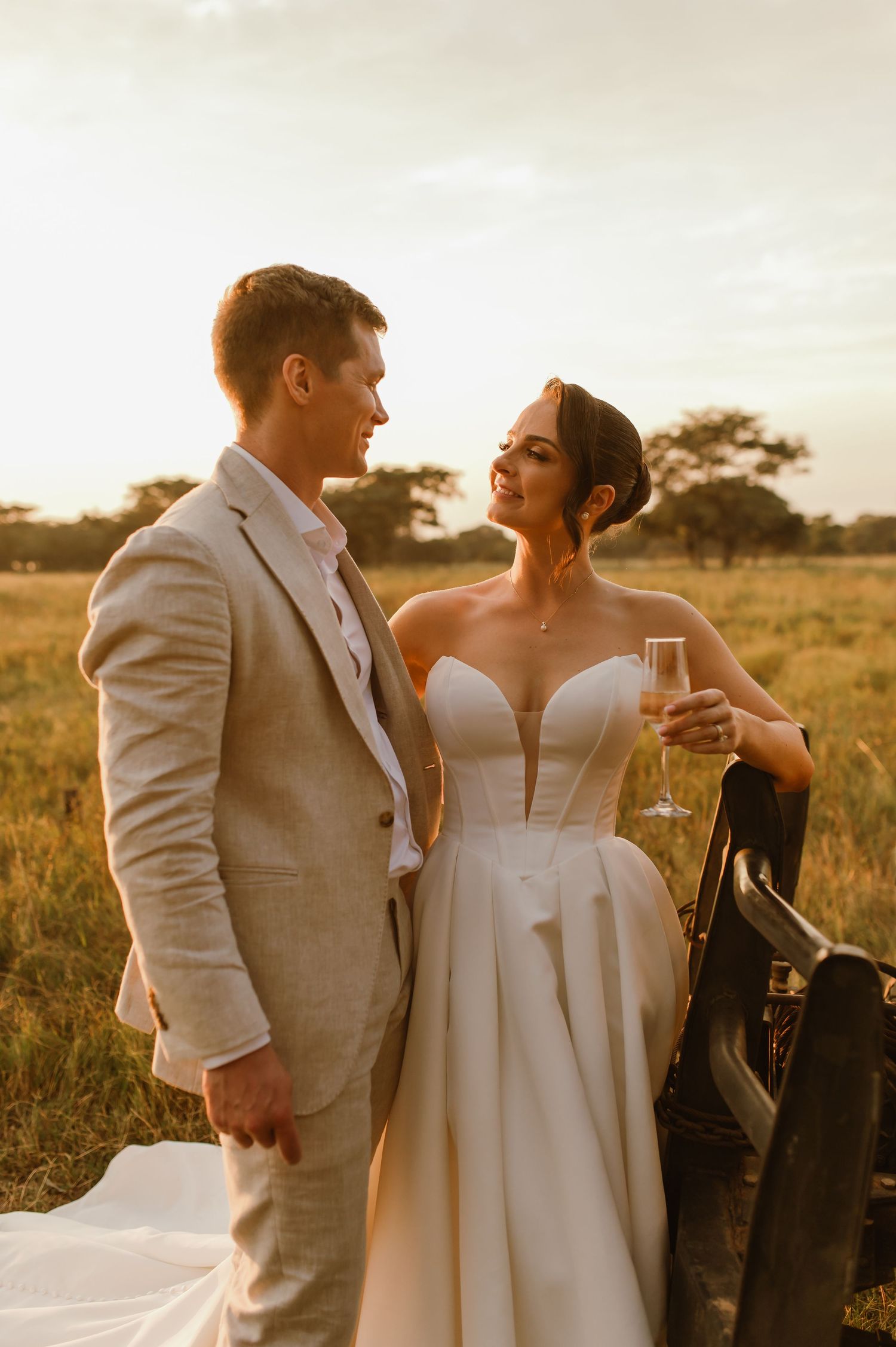 Newlyweds enjoy drinks together during golden hour in an outdoor setting.