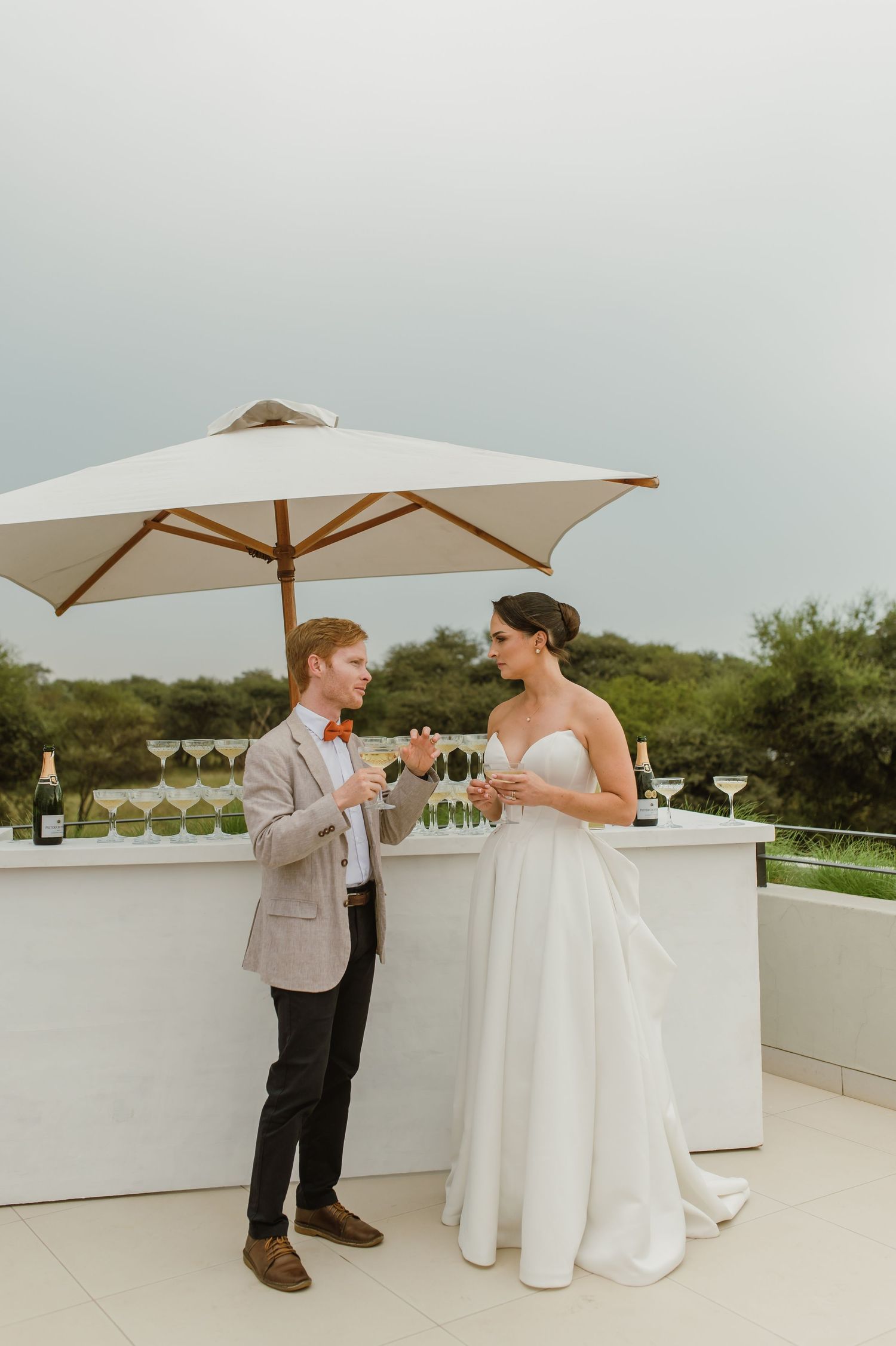 A couple shares an intimate moment on an outdoor rooftop terrace with white tables and umbrellas.