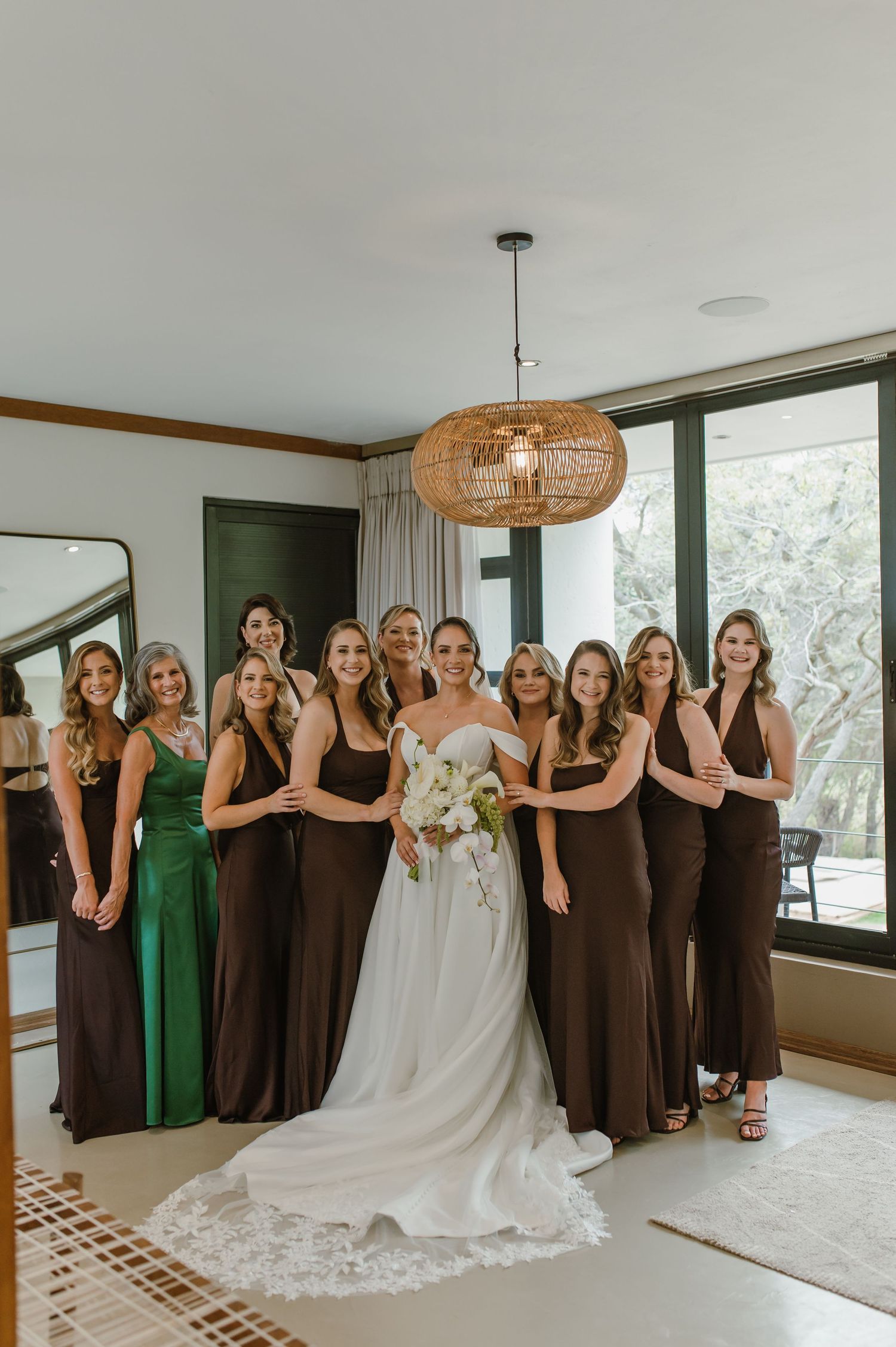 Wedding party group photo with bridesmaids in brown and green dresses alongside bride in white gown.