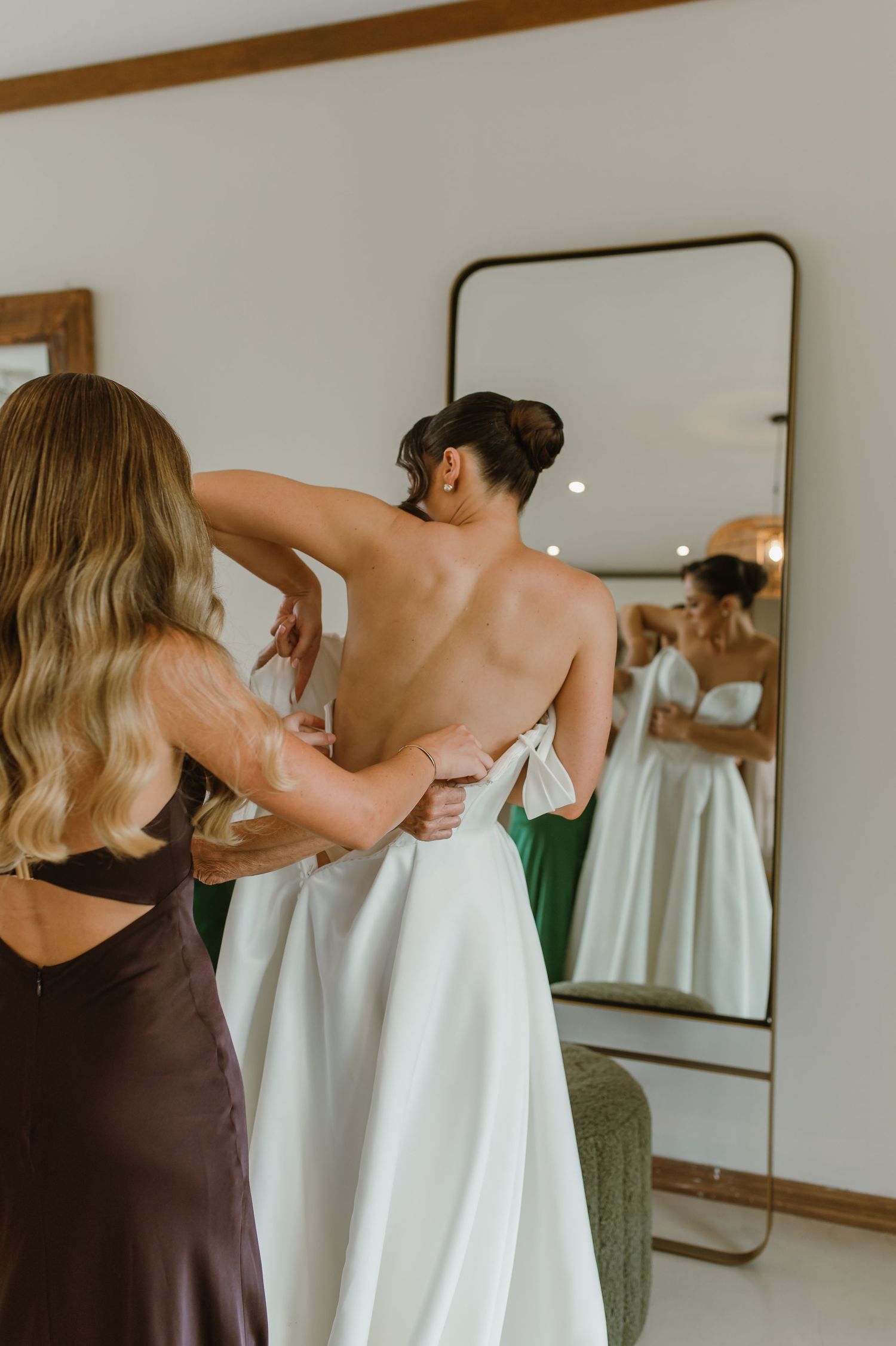 A group getting ready in a room with mirrors and brown dresses preparing for a formal event.