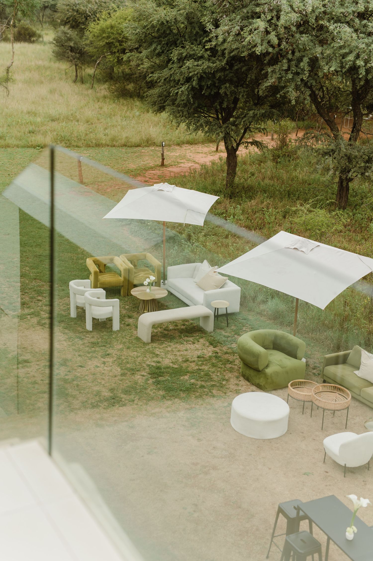 Modern outdoor lounge area with white furniture and umbrellas arranged on a patio surrounded by greenery.