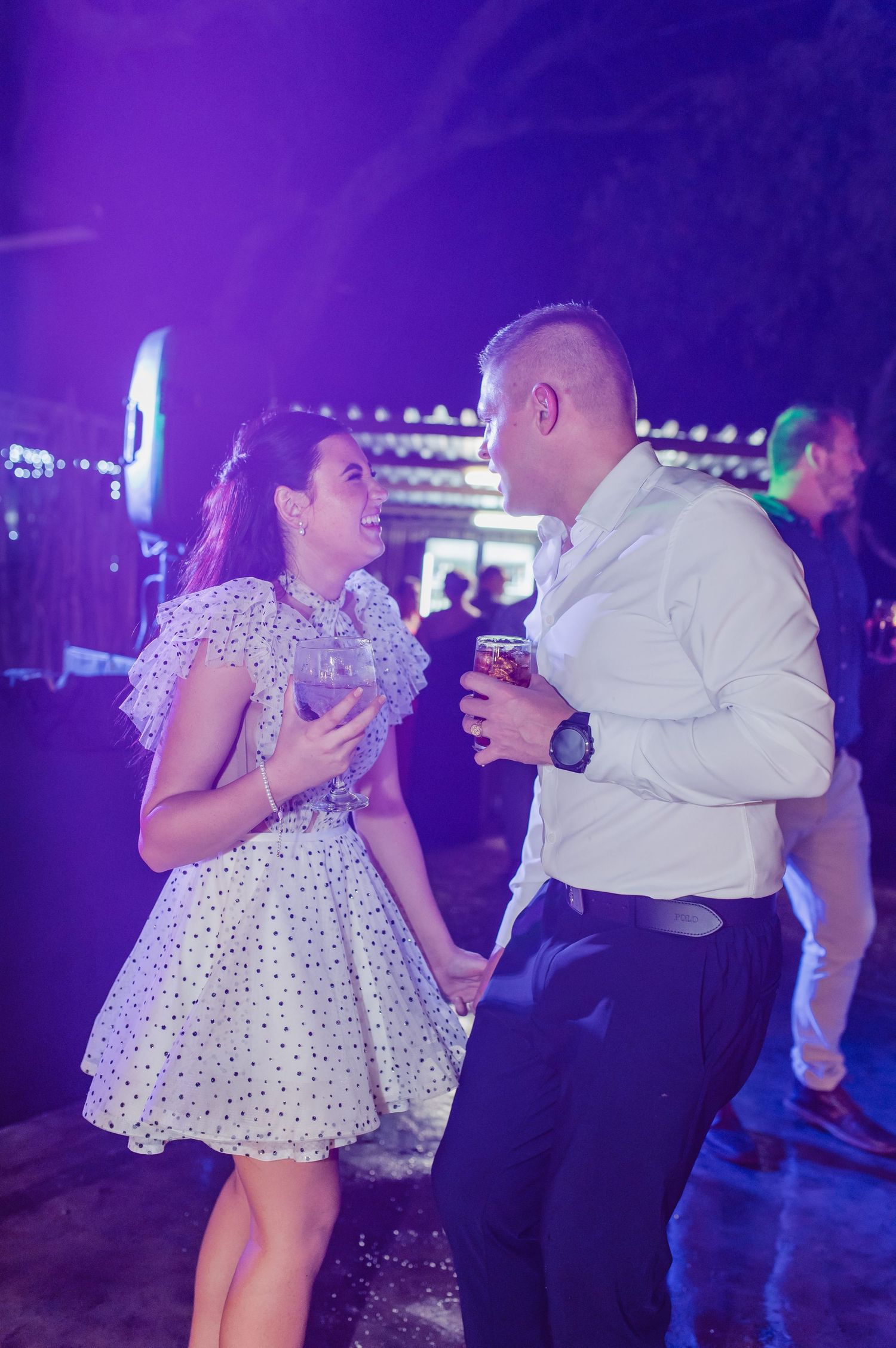 Couple dancing and laughing together under purple lights at a lively wedding reception.