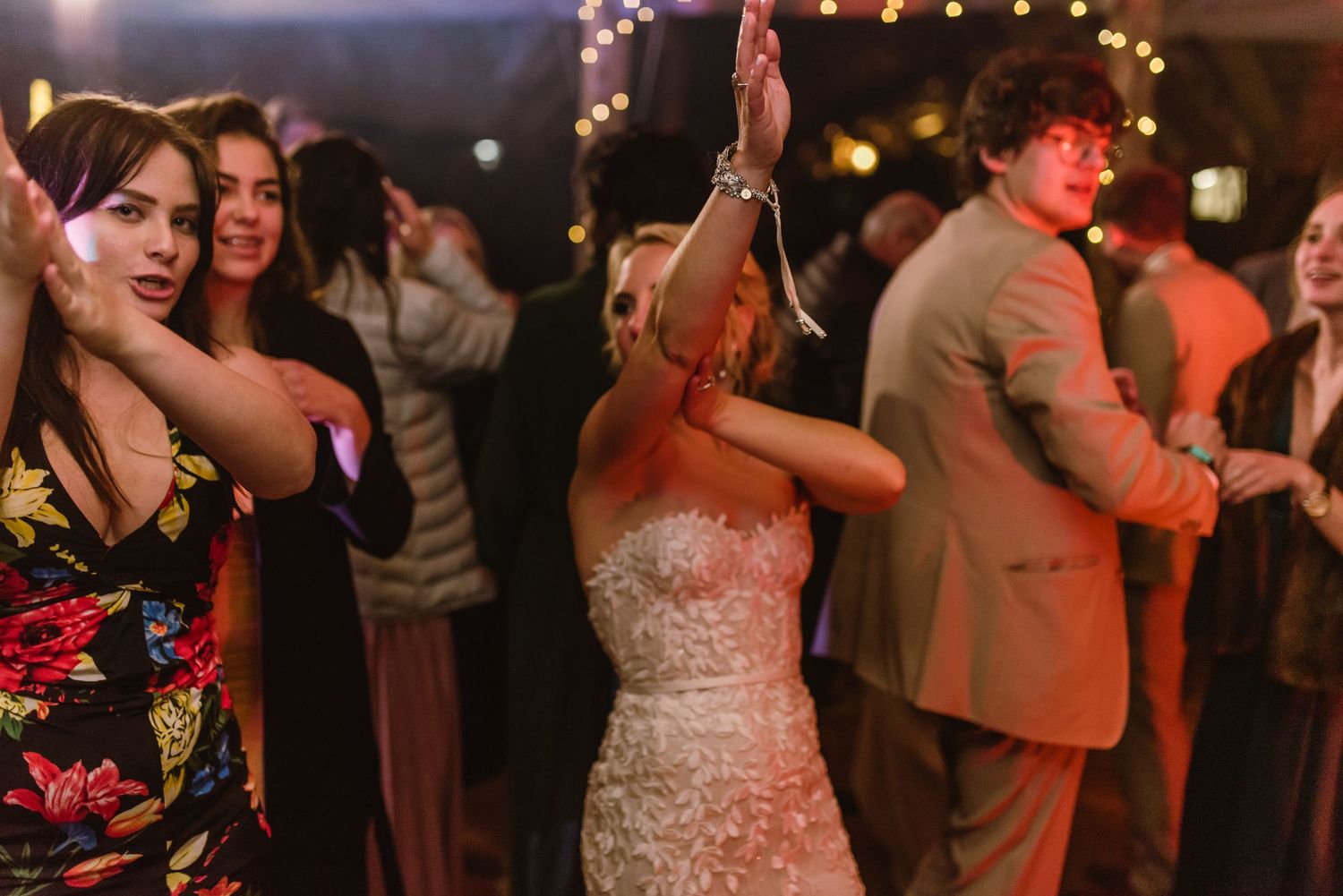 Energetic dance party at a wedding reception with guests enjoying themselves under decorative lighting.