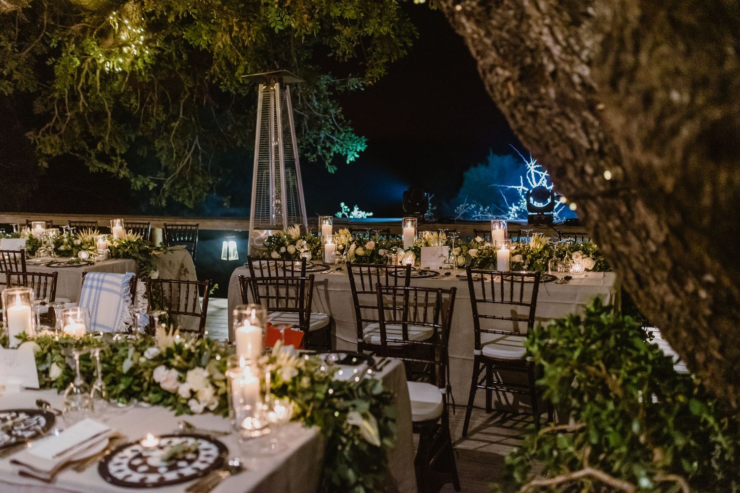 Outdoor reception area with elegant table settings beneath tree canopy.