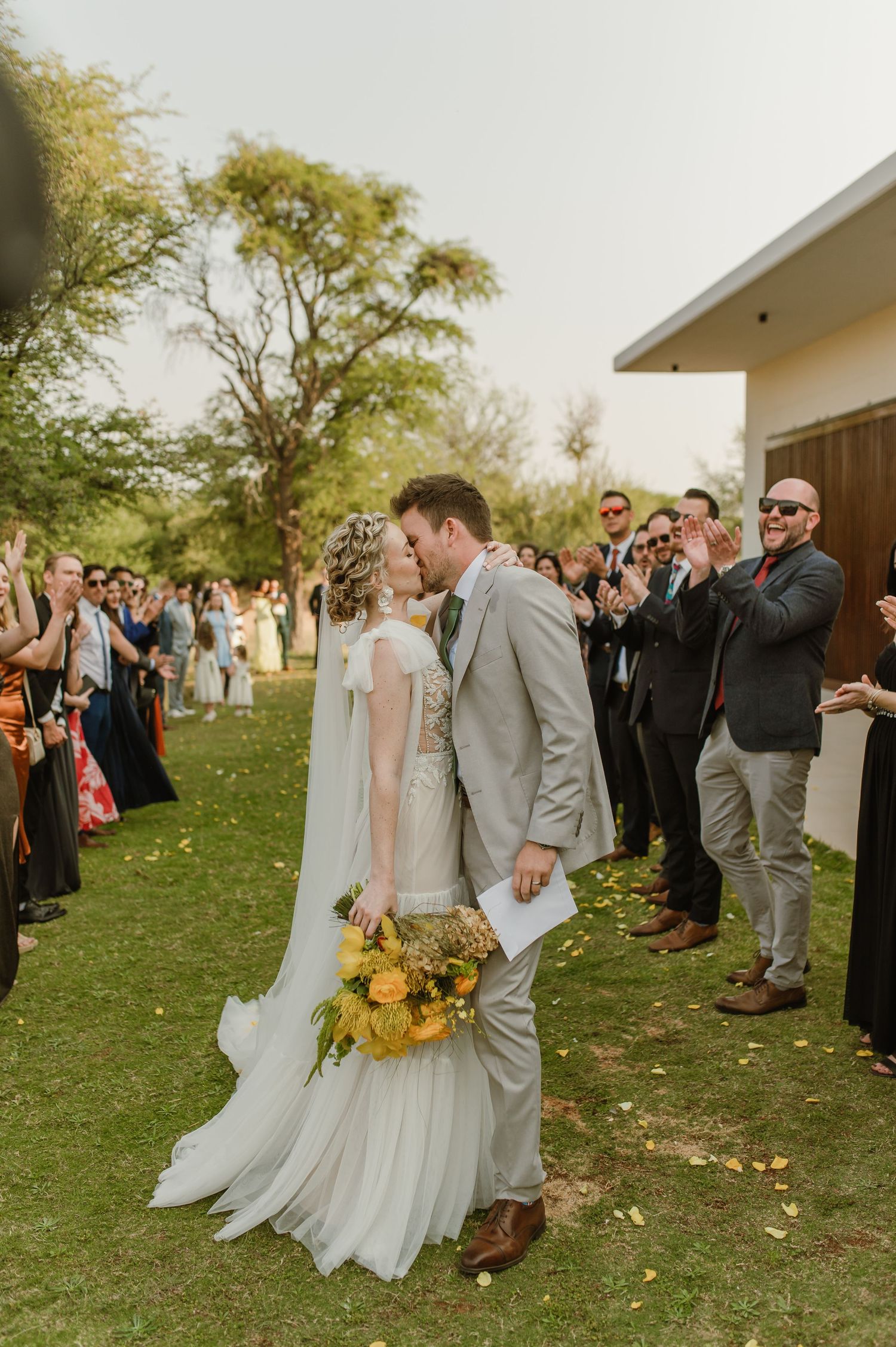 Wedding party walking through outdoor venue with guests celebrating and throwing confetti.