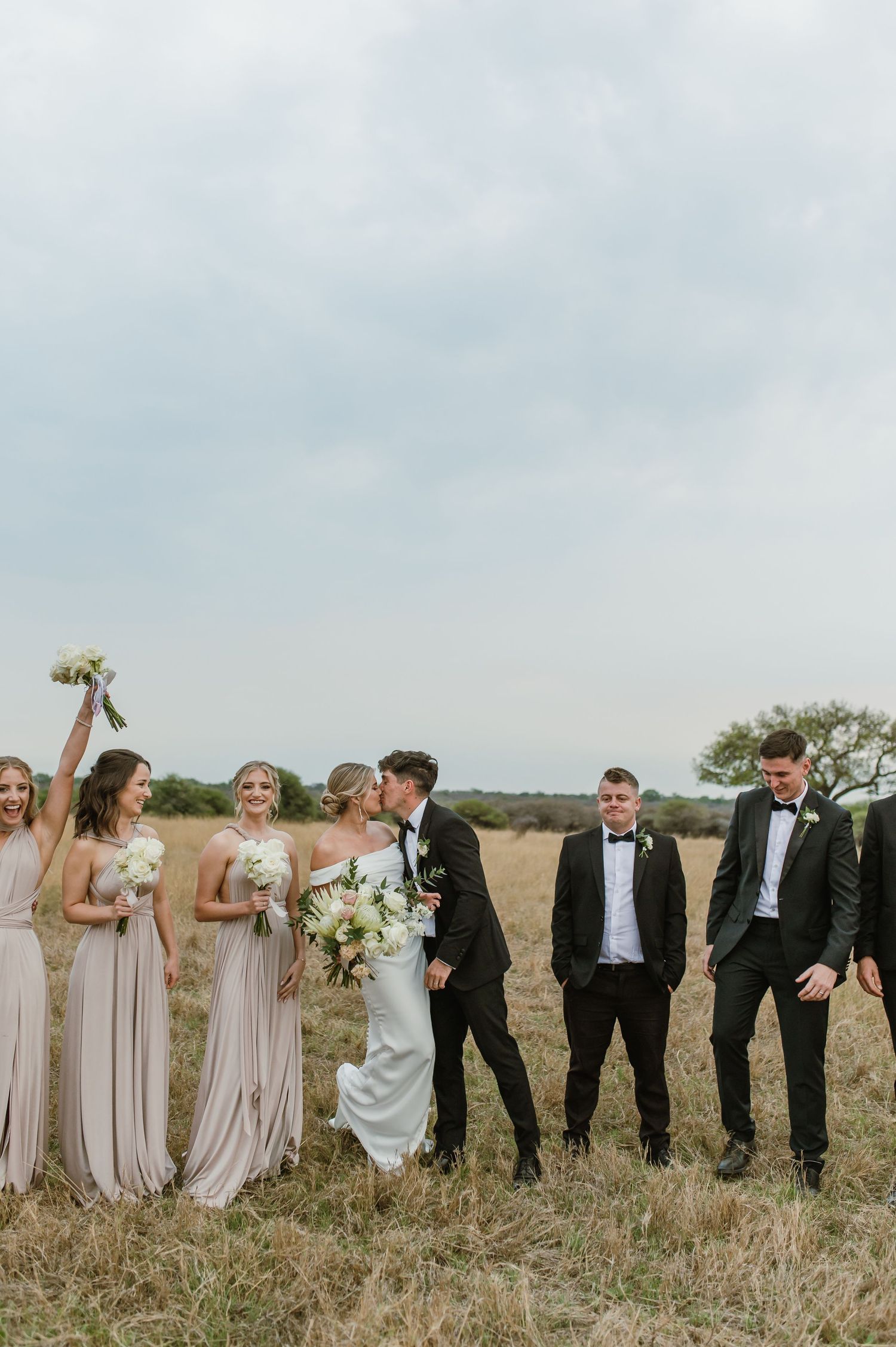 Bridal party celebrates joyfully in a rustic field setting.