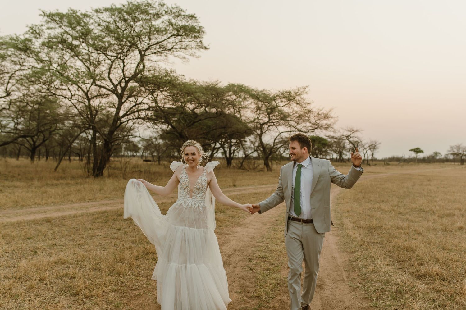 Joyful wedding couple dances and celebrates in an open field during golden hour.