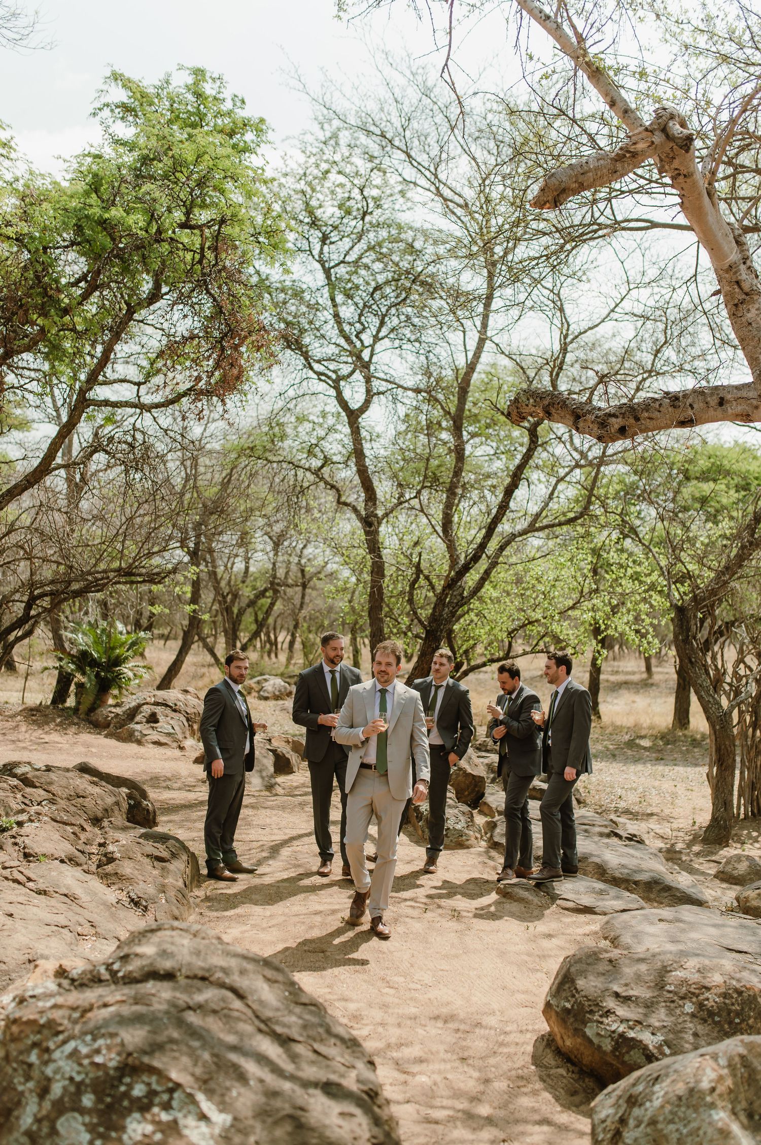 Wedding party gathered on rocky terrain surrounded by trees.