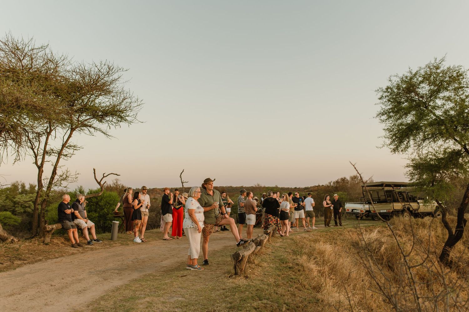 Safari group gathered on dirt path during sunset game drive stop.