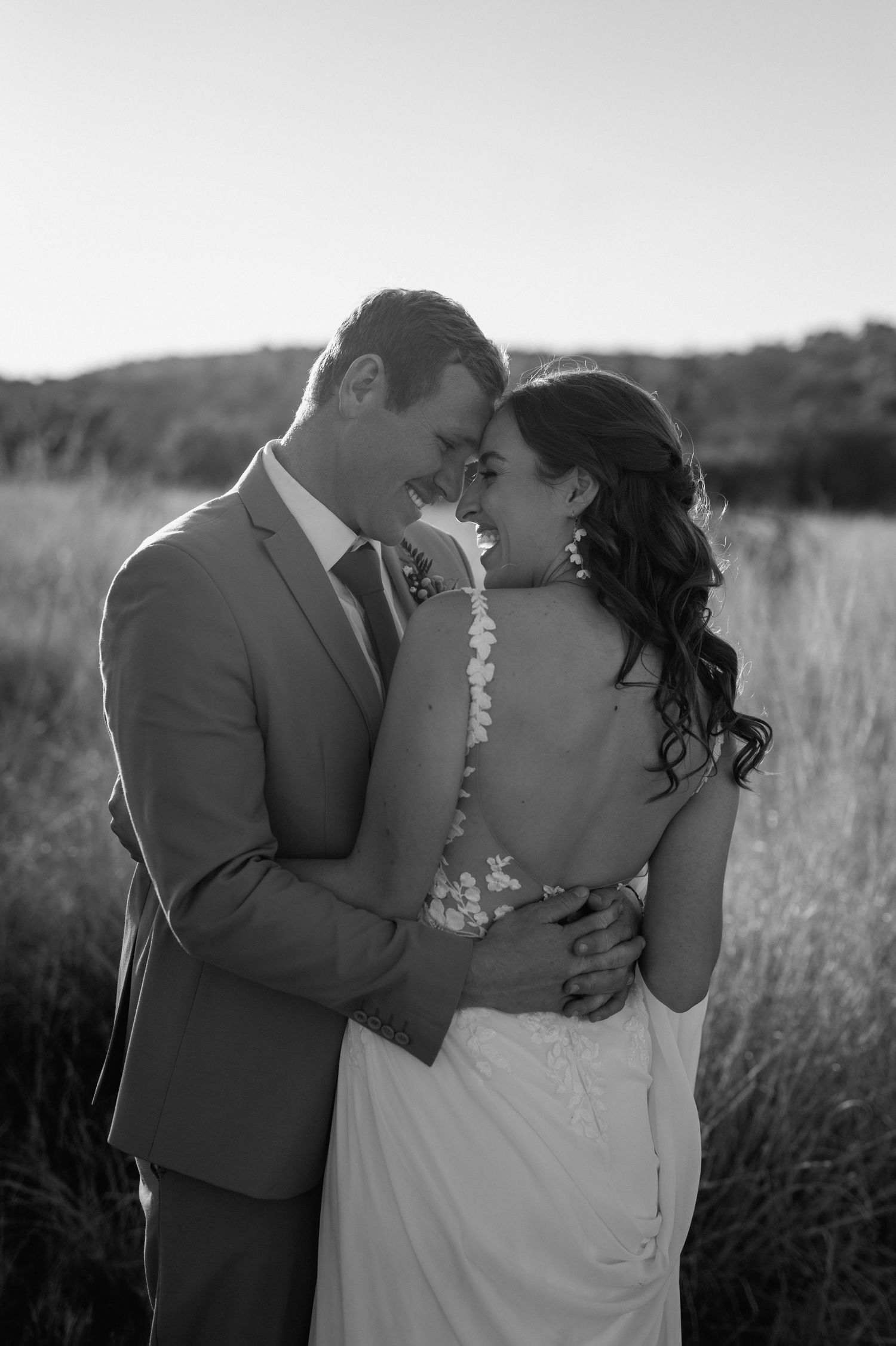 Black and white intimate wedding portrait of a couple embracing in a field at sunset.