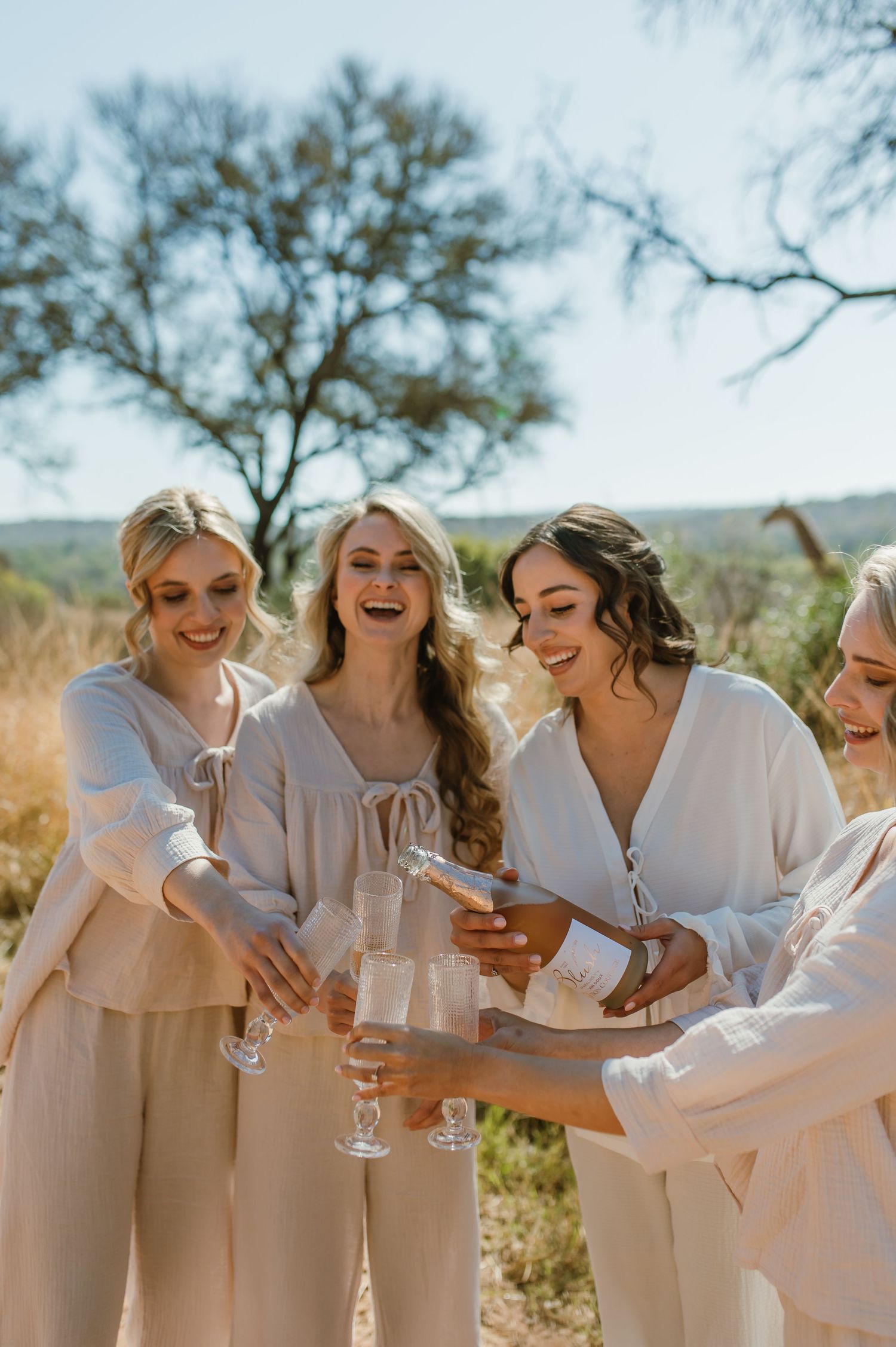 Friends in white outfits laughing together outdoors on sunny day.