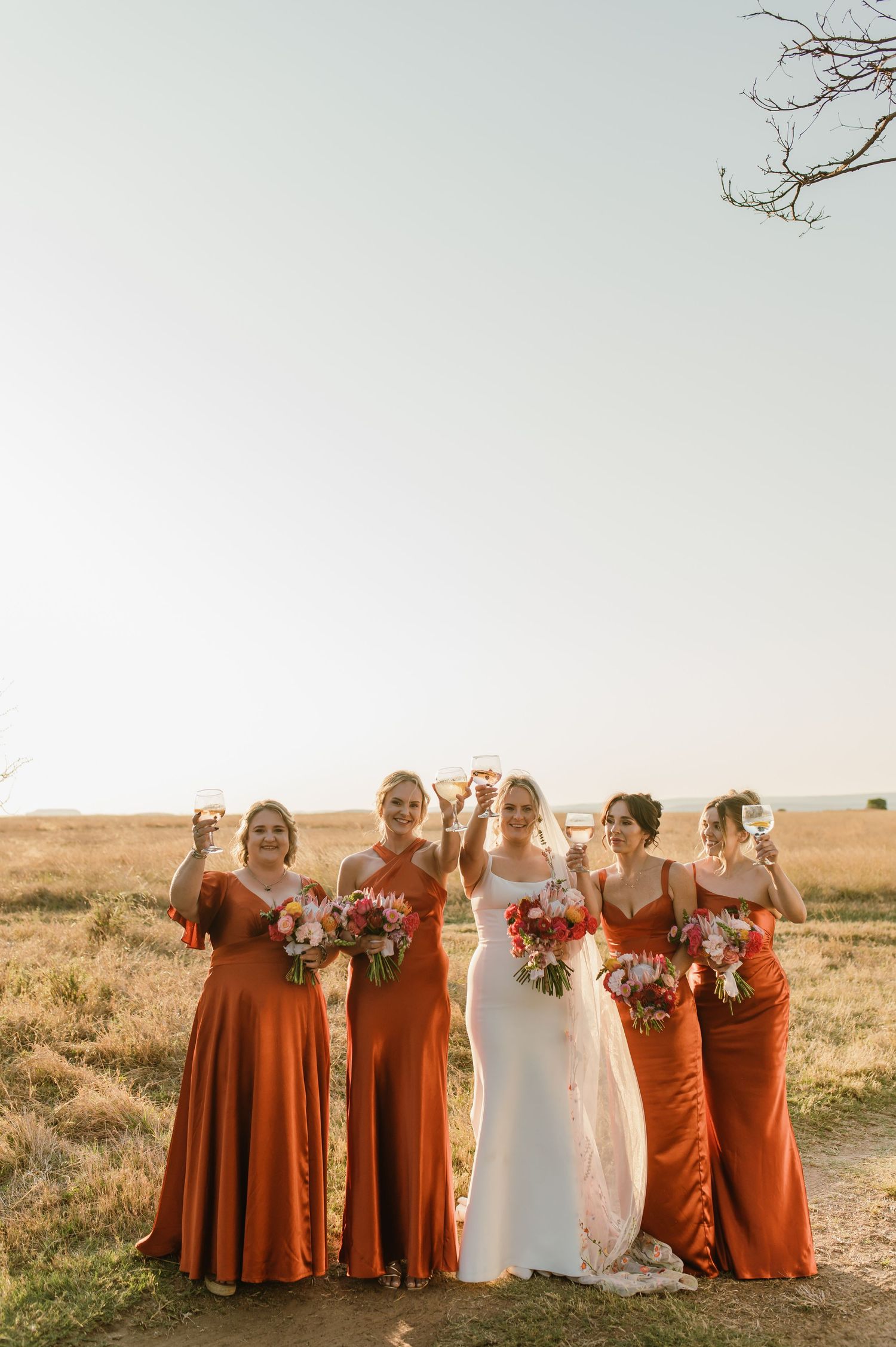 Bridal party wearing rust-colored dresses stands together in a desert landscape.