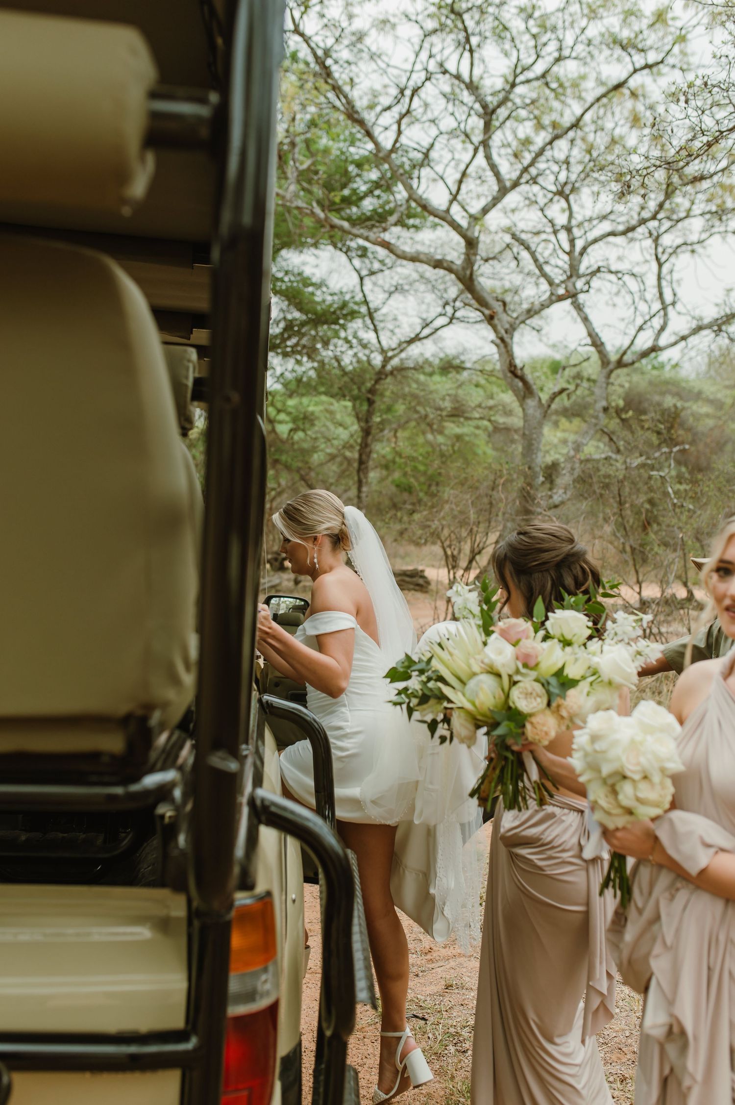 Bridal party with bouquets preparing to board vehicle in natural outdoor setting.