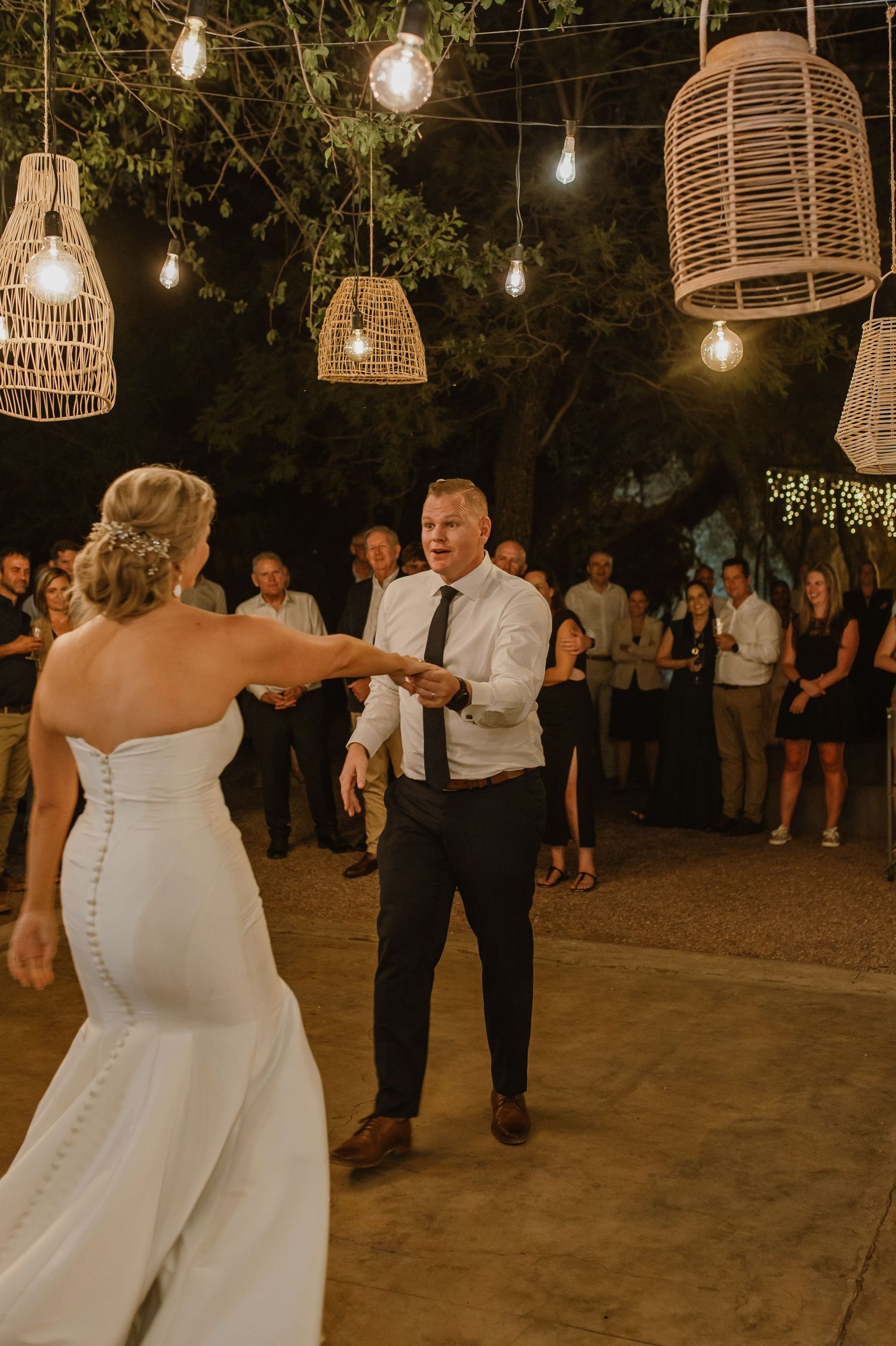Wedding couple shares intimate dance moment under rustic outdoor lighting and woven lantern decor.