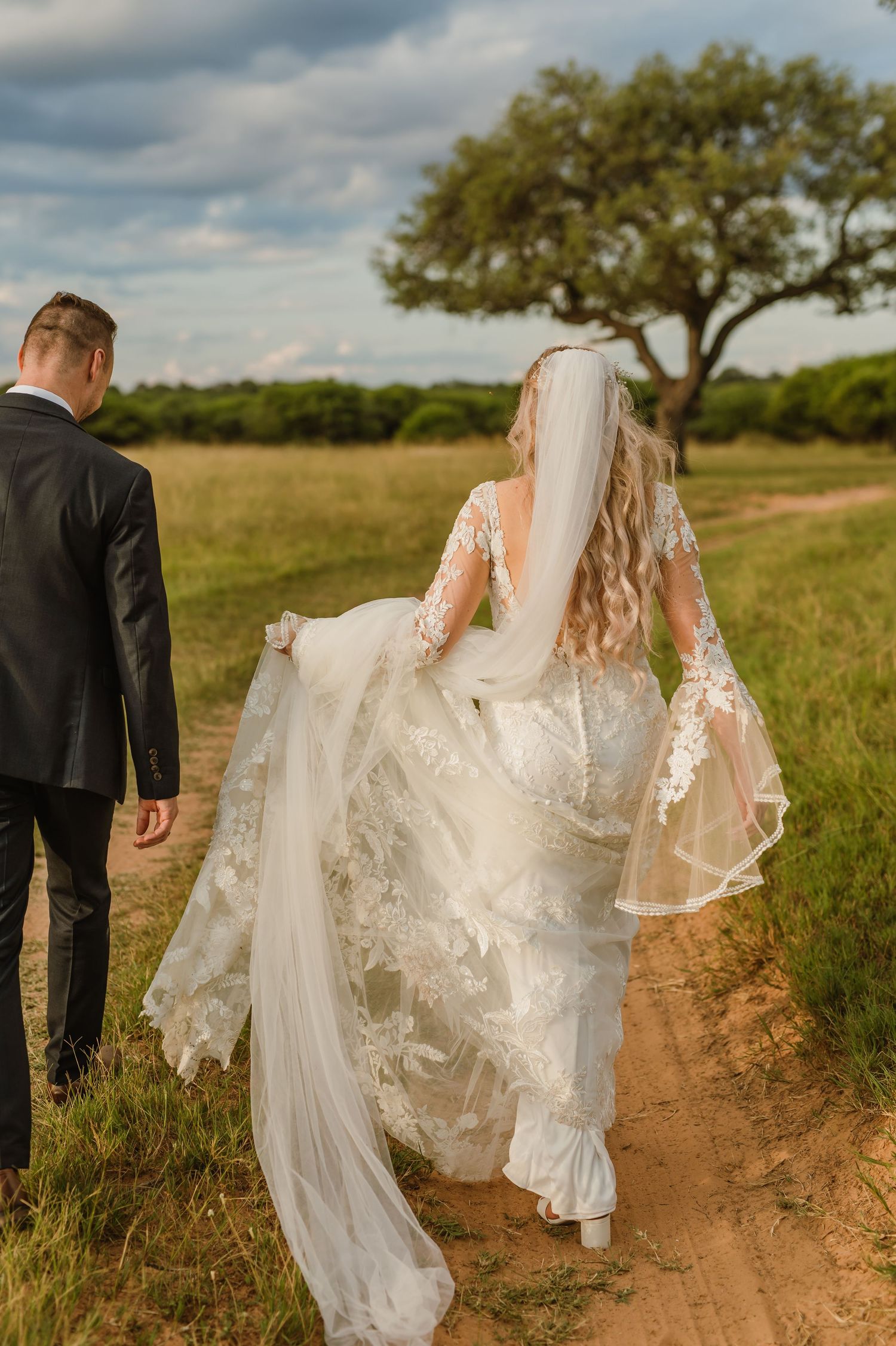 Wedding couple walking down a winding dirt path with oak trees in the background.