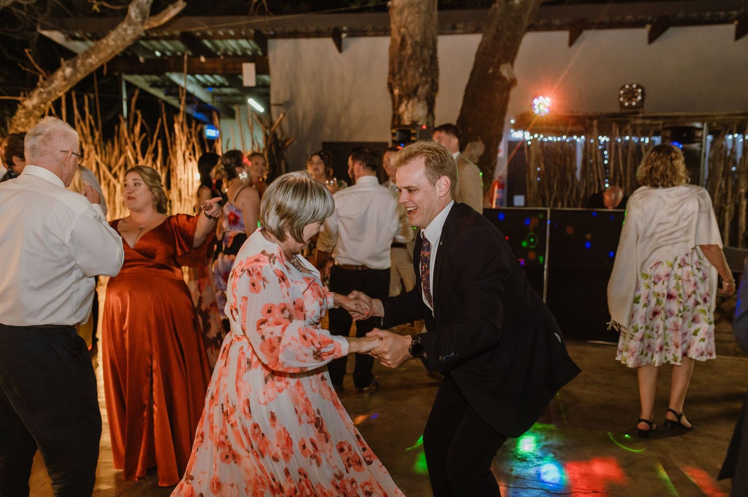 Wedding guests dancing and mingling at an outdoor reception with ambient lighting.