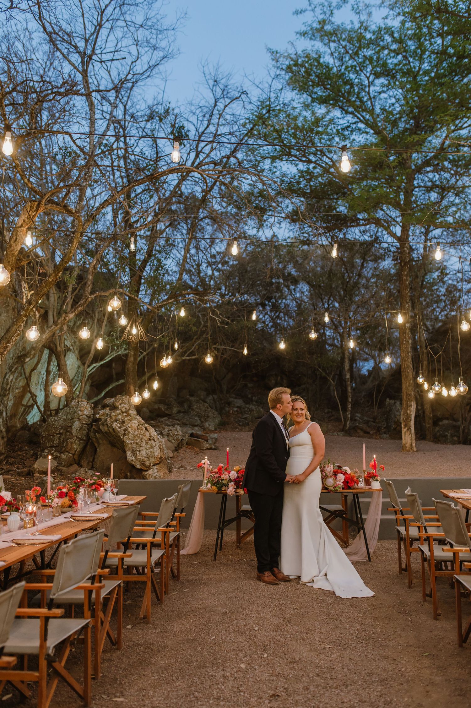 An outdoor wedding reception setup with string lights and rustic wooden tables.