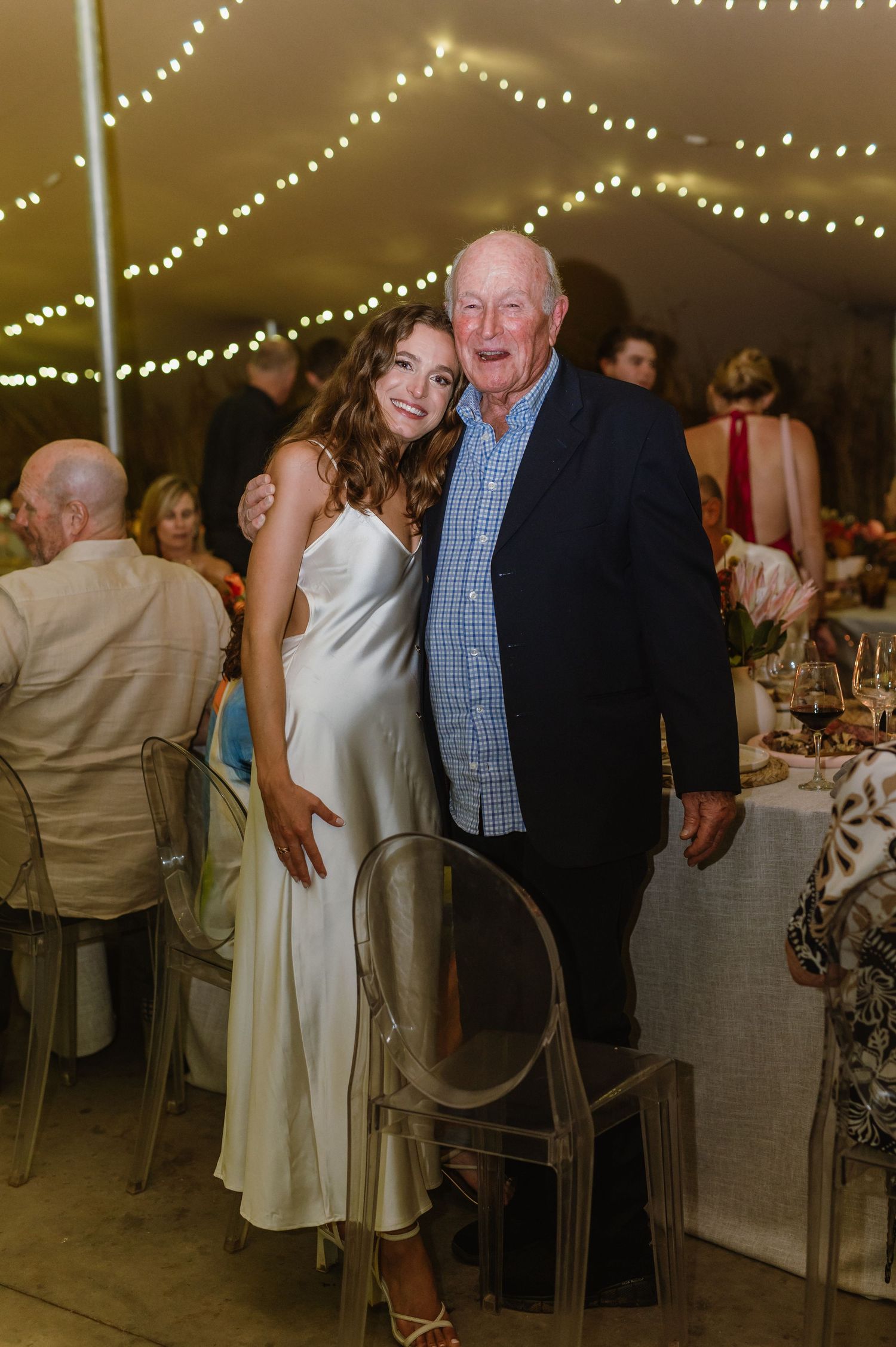 Evening wedding reception with guests mingling under string lights in an elegant tent setting.