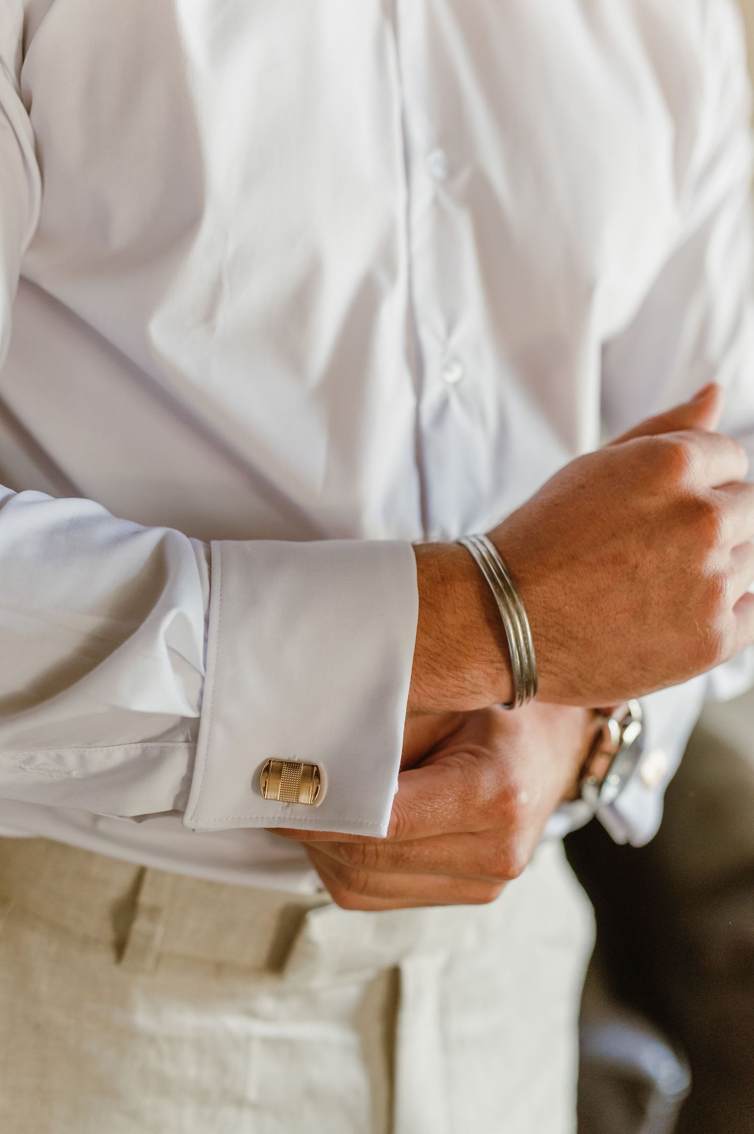 Close-up shots of hands fastening gold cufflinks on a formal white shirt sleeve.
