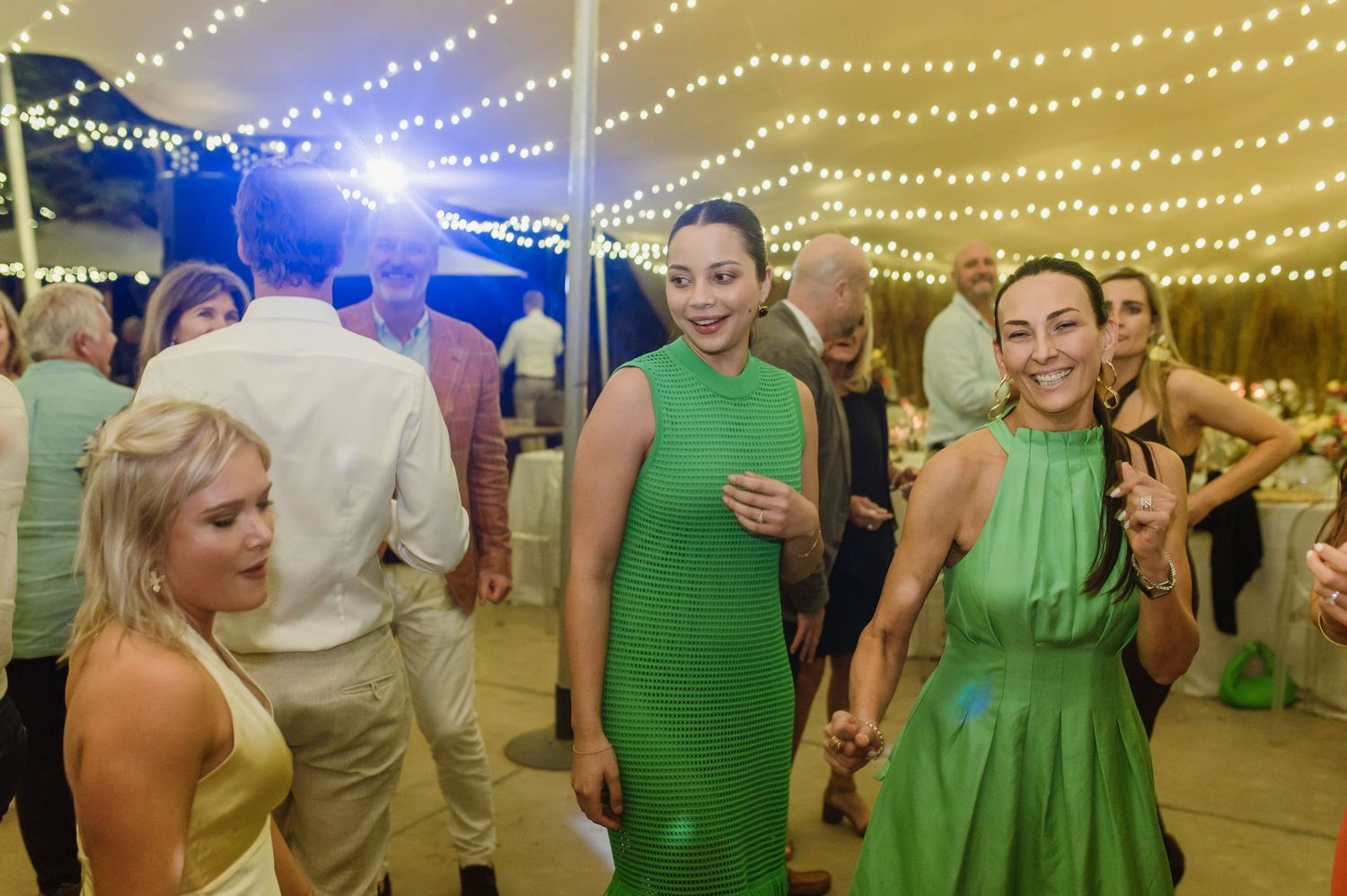 Wedding reception dance floor filled with guests celebrating under warm string lights and blue accents.