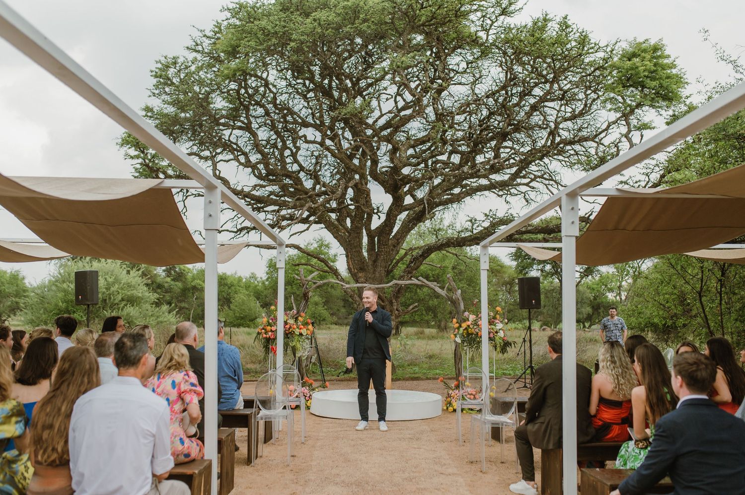 Wedding ceremony setup with white canopy and rows of seating under natural tree cover.