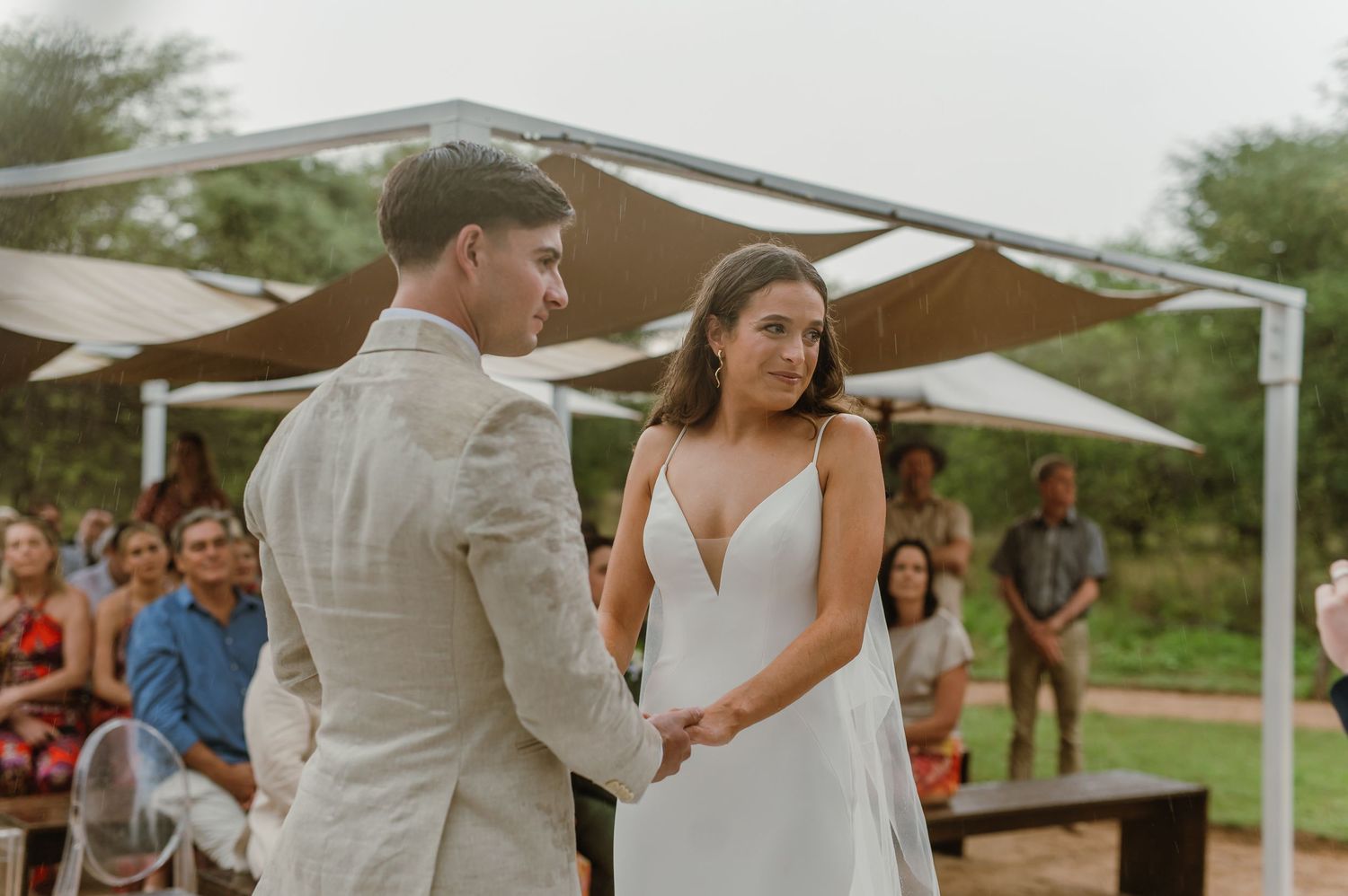 Couple exchanges vows during outdoor desert wedding ceremony under white canopy structure.