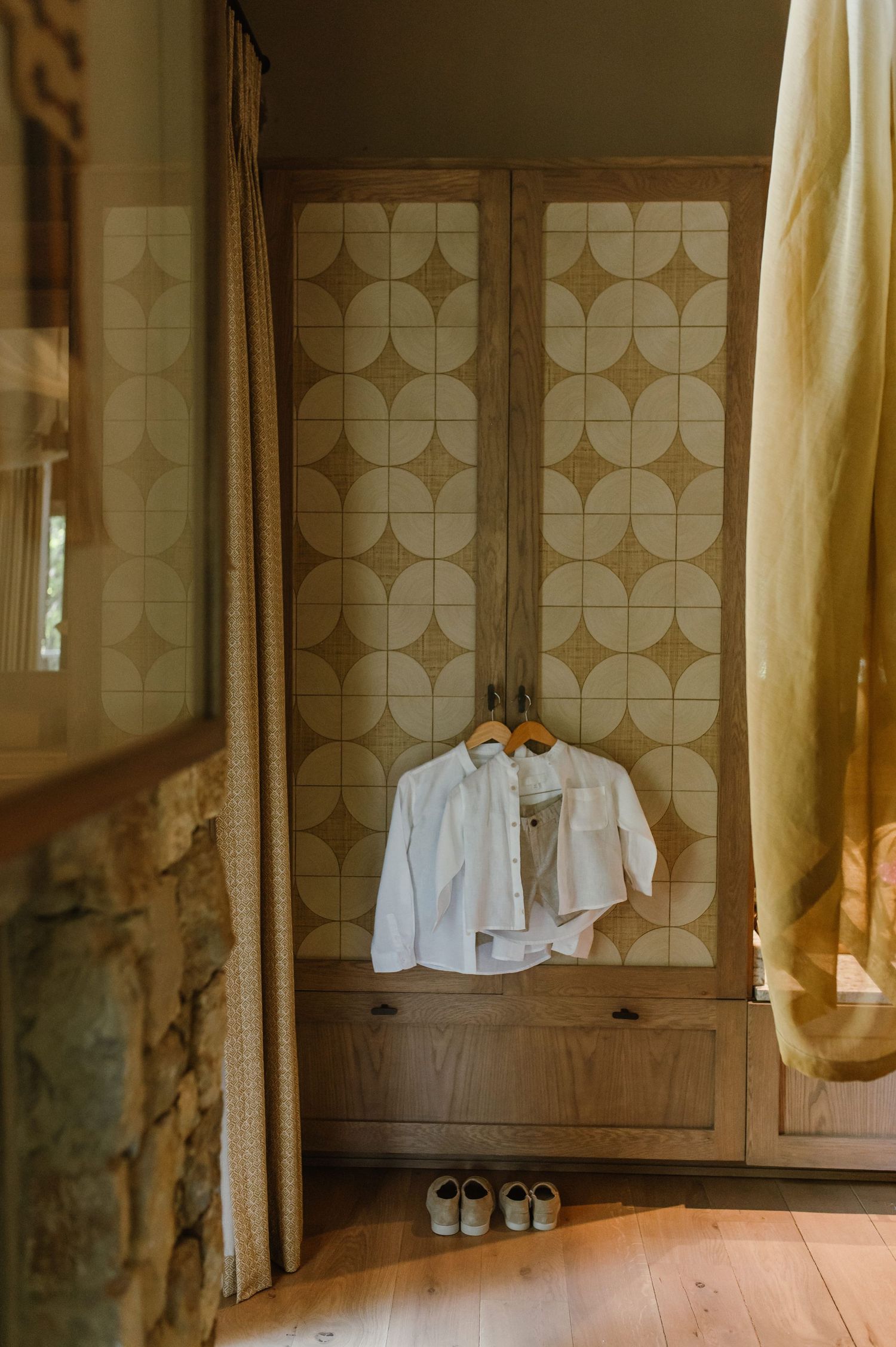 White shirts hanging on wooden wardrobe with geometric tile doors, shoes below on hardwood floor.