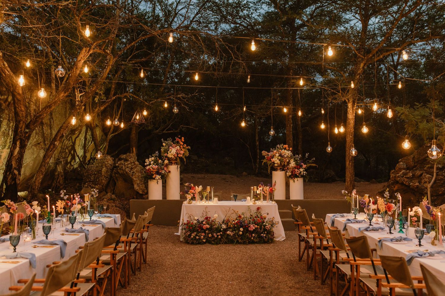 Magical outdoor wedding reception with Edison bulb string lights, floral centerpieces, and candlelit tables.