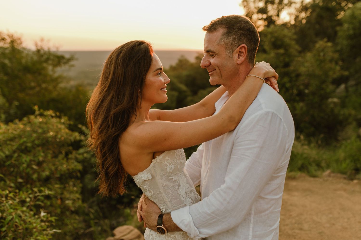 Smiling bride and groom embrace and gaze at each other during a romantic golden hour outdoor wedding.