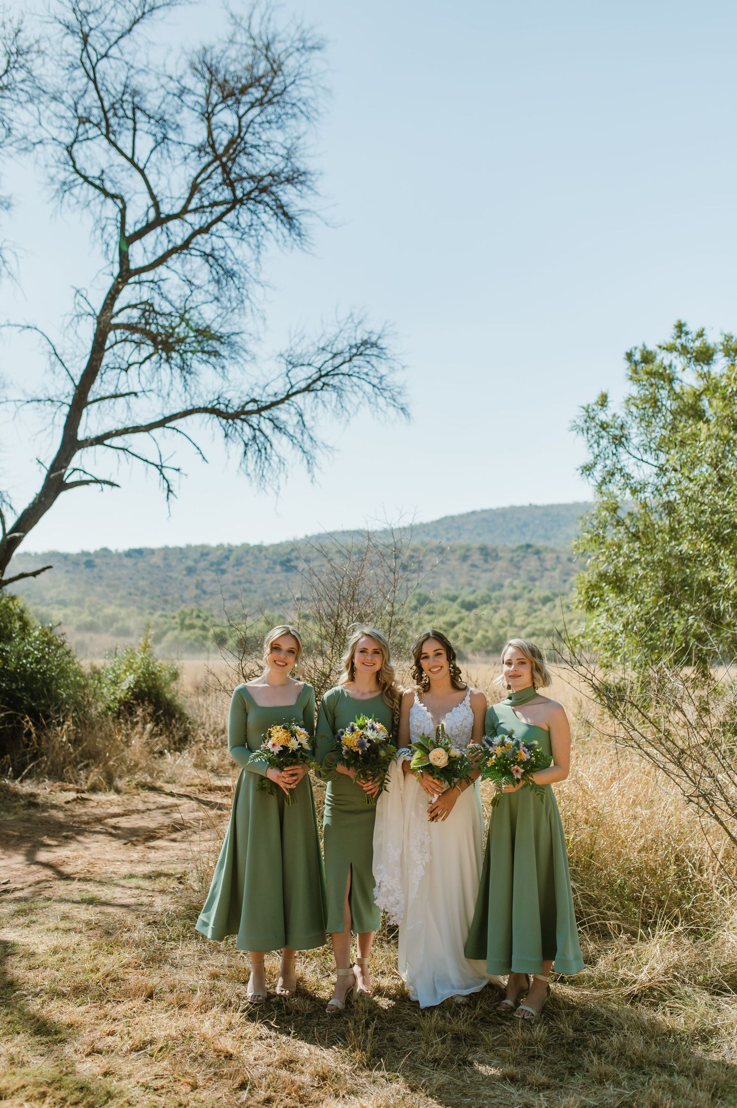 Wedding party poses in sage green bridesmaid dresses and white bridal gown against desert mountain backdrop.