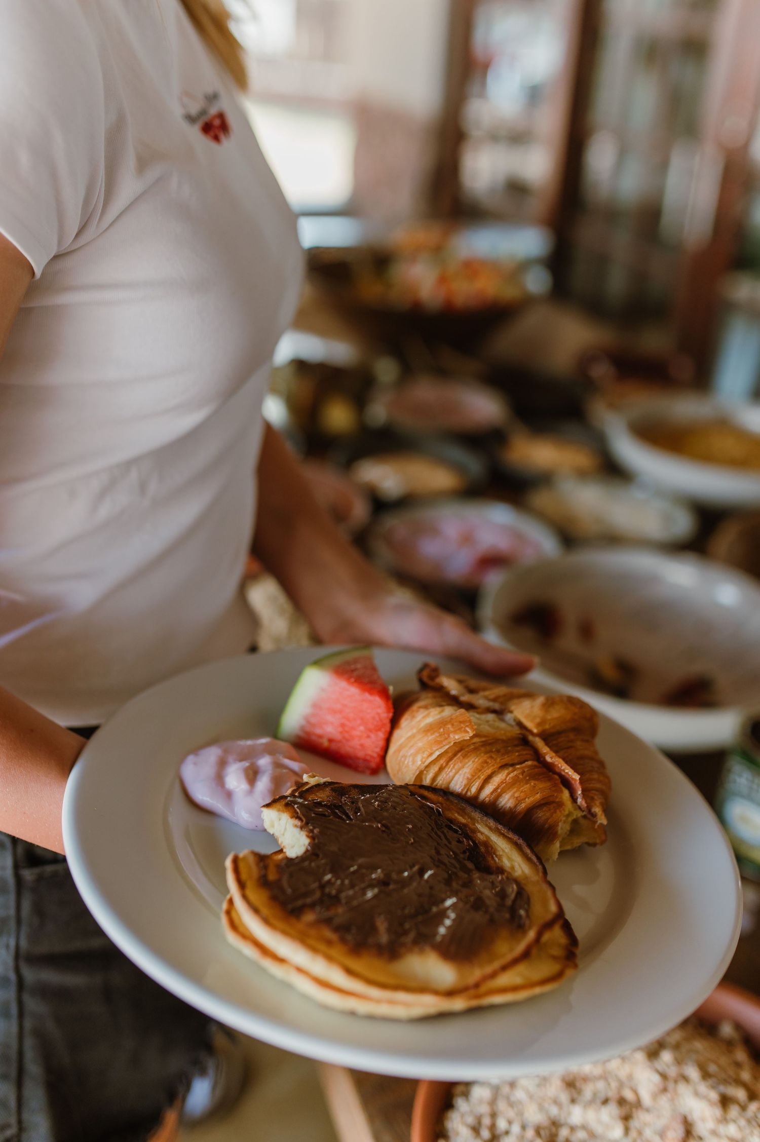 White plates of chocolate-topped pancakes and breakfast items being served at a wedding reception.