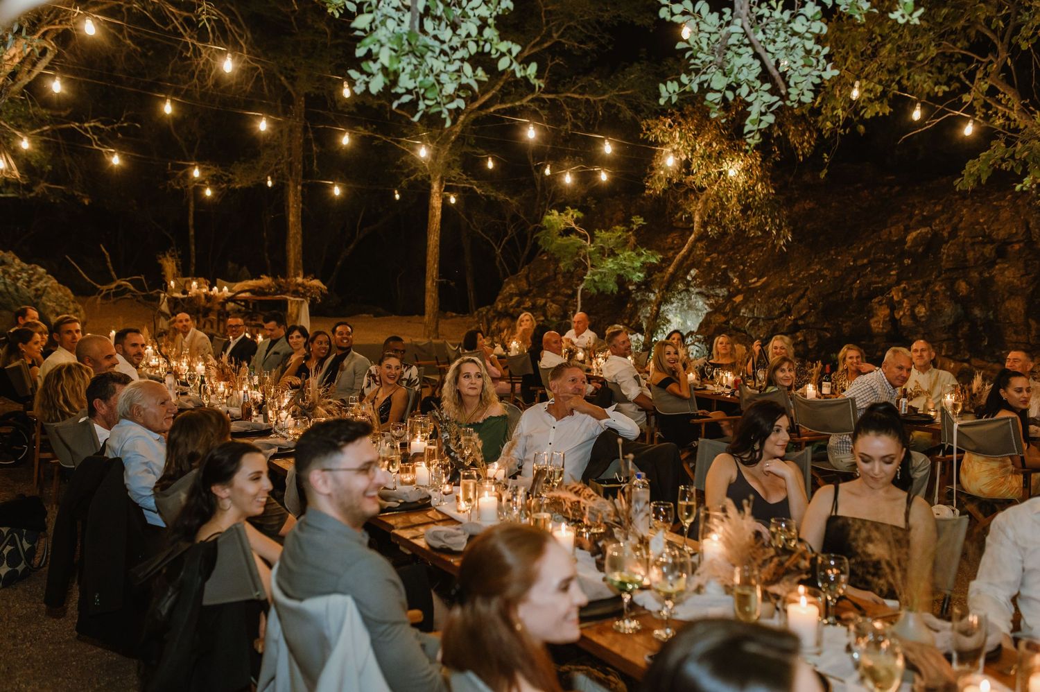 Festive outdoor evening reception with string lights illuminating tables and dancing guests.