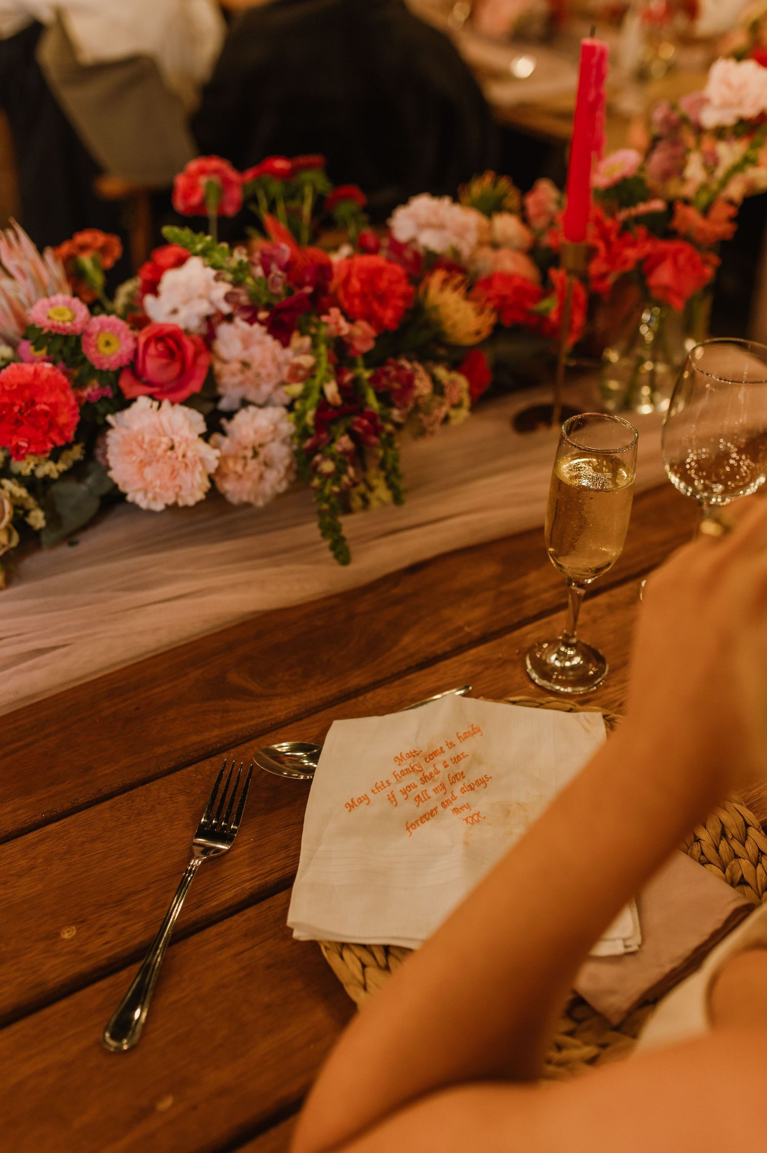 Rustic wooden table decorated with red and pink floral arrangements and glowing candlelight for an intimate dinner setting.