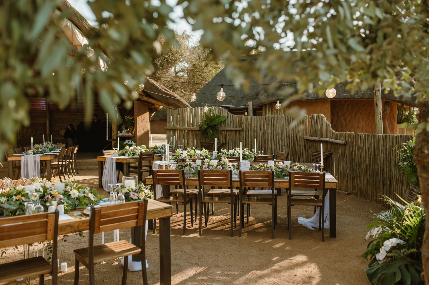 Intimate outdoor dining setup with wooden tables and chairs surrounded by natural desert vegetation.