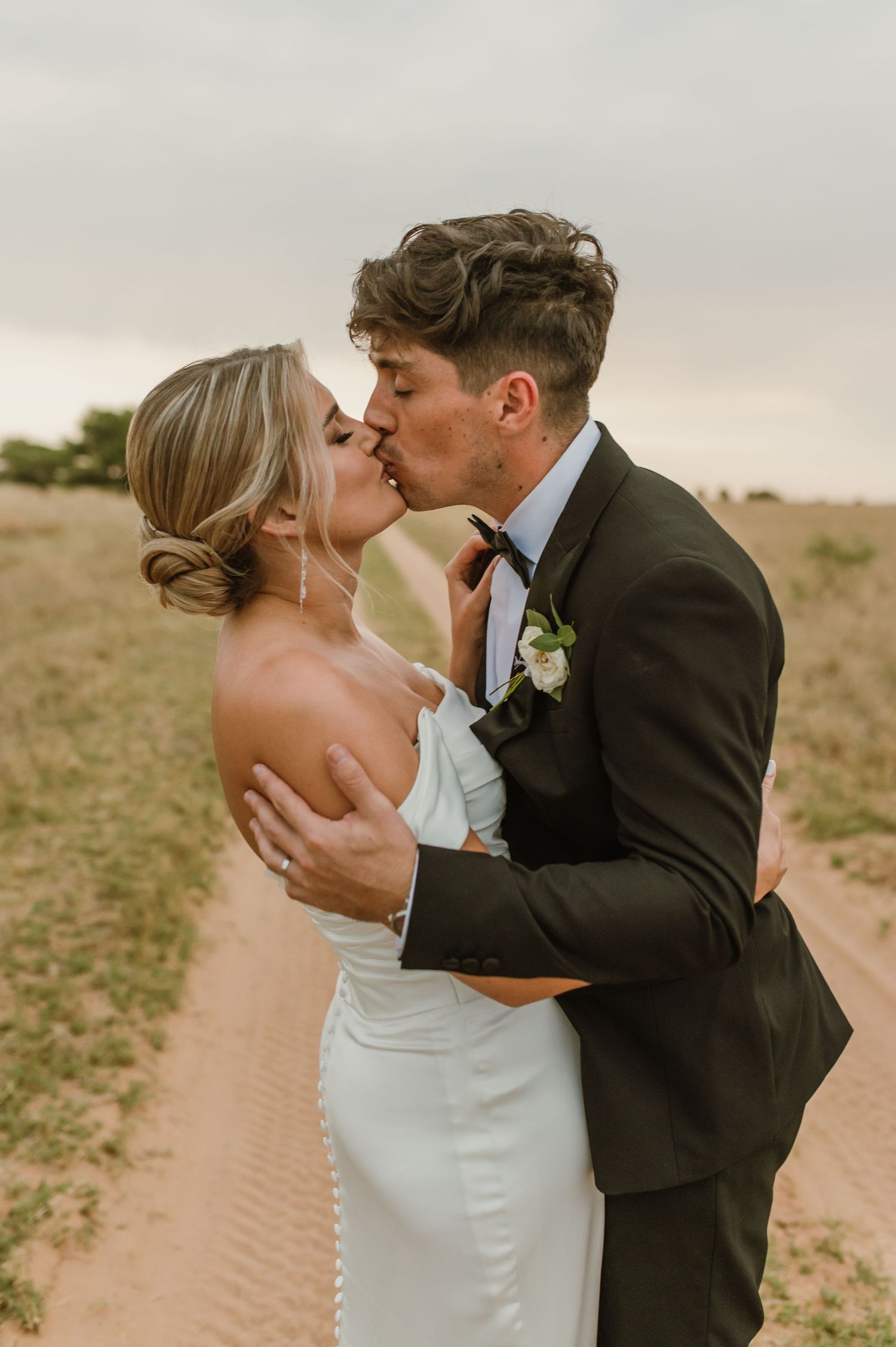 Romantic sunset wedding photos showing intimate kisses between a couple on a dirt path.