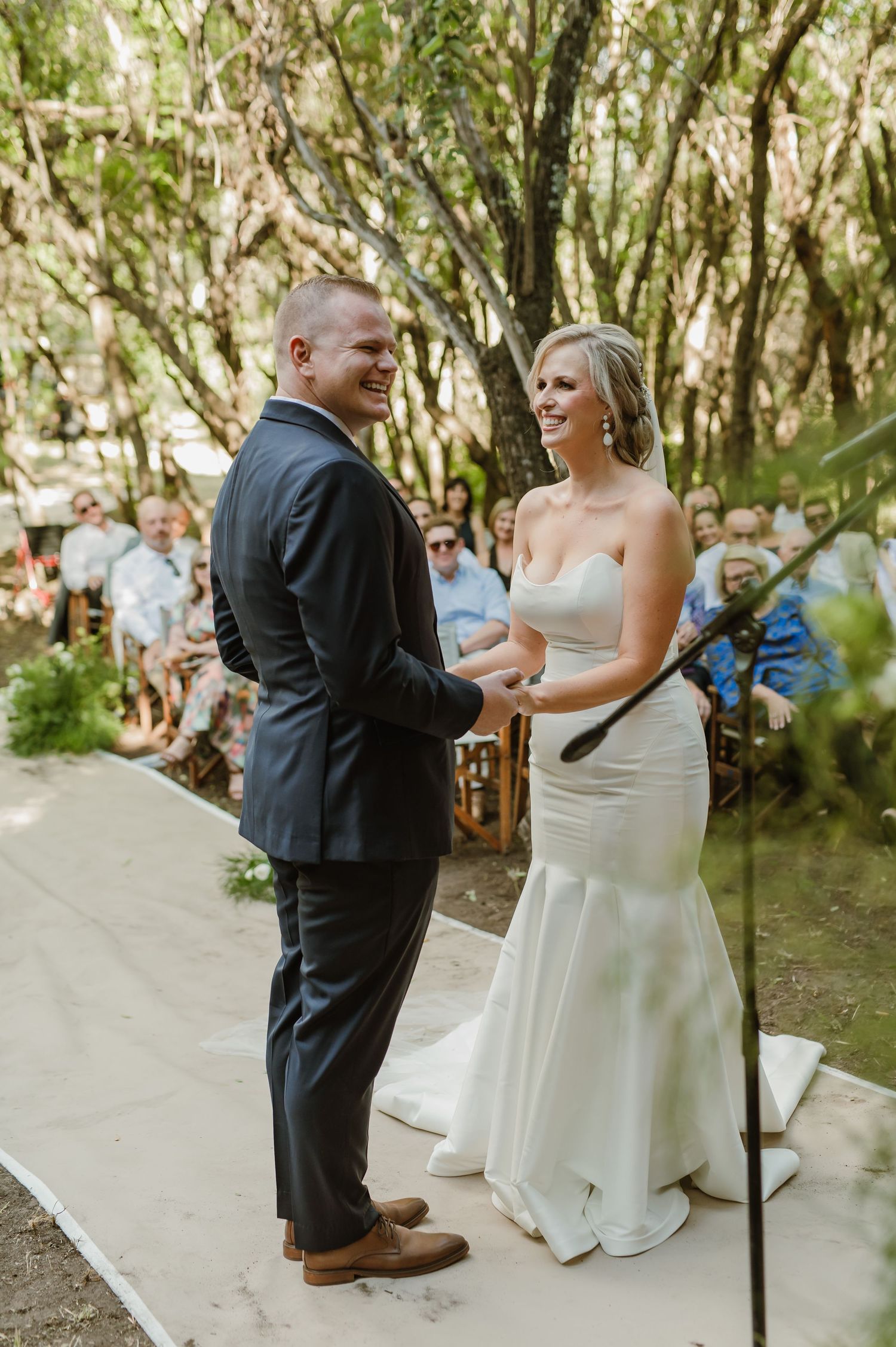 A wedding ceremony unfolds on a white aisle runner surrounded by natural forest scenery.